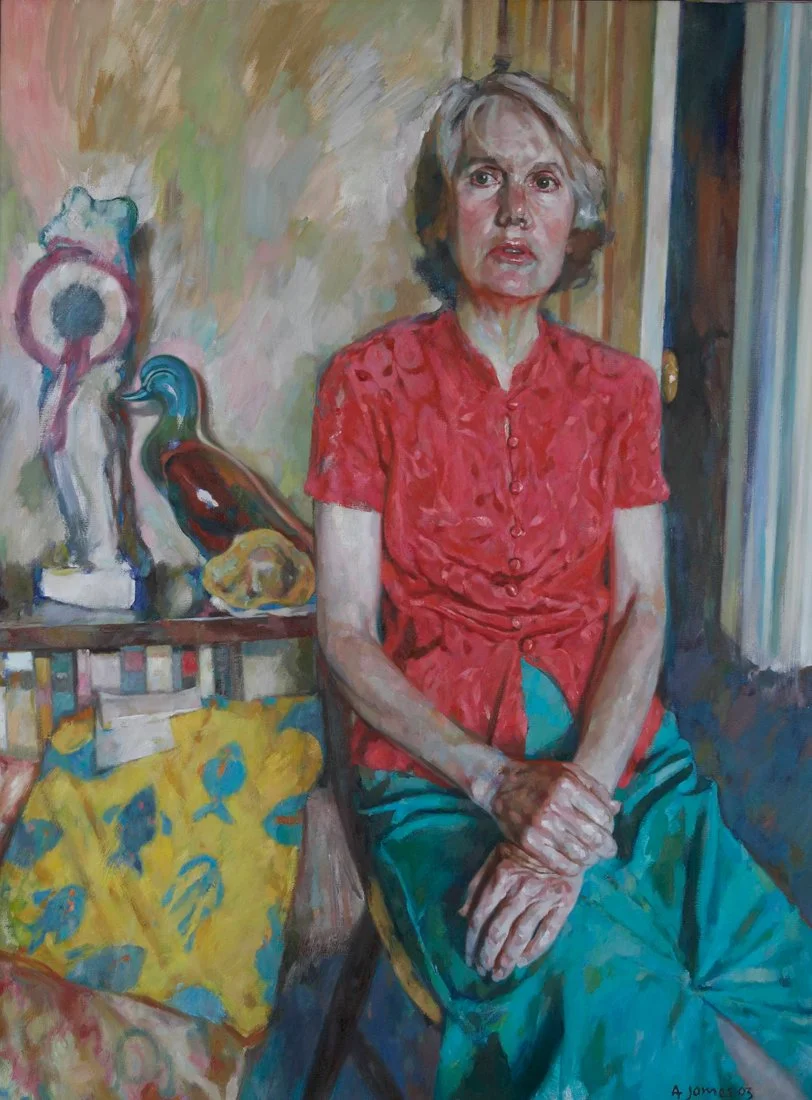 A painting of a woman with gray hair wearing a red shirt and green pants, sitting on a chair in a room with colorful decor, including sculptures and a yellow cloth with blue patterns on a table beside her.