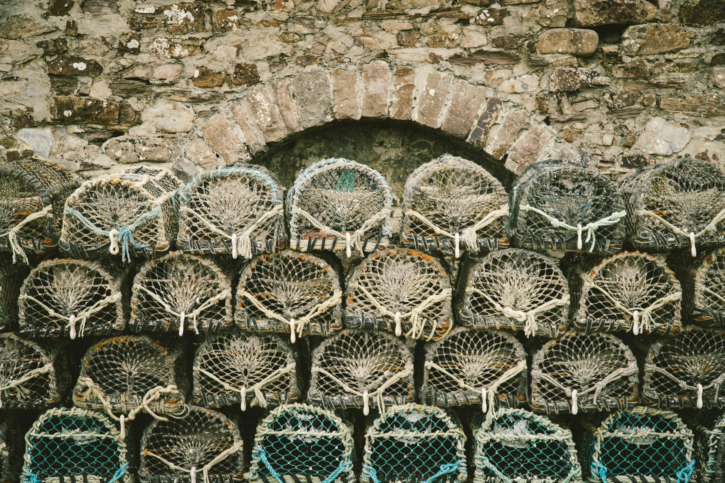 Stacked fishing pots against a stone wall in Cornwall.