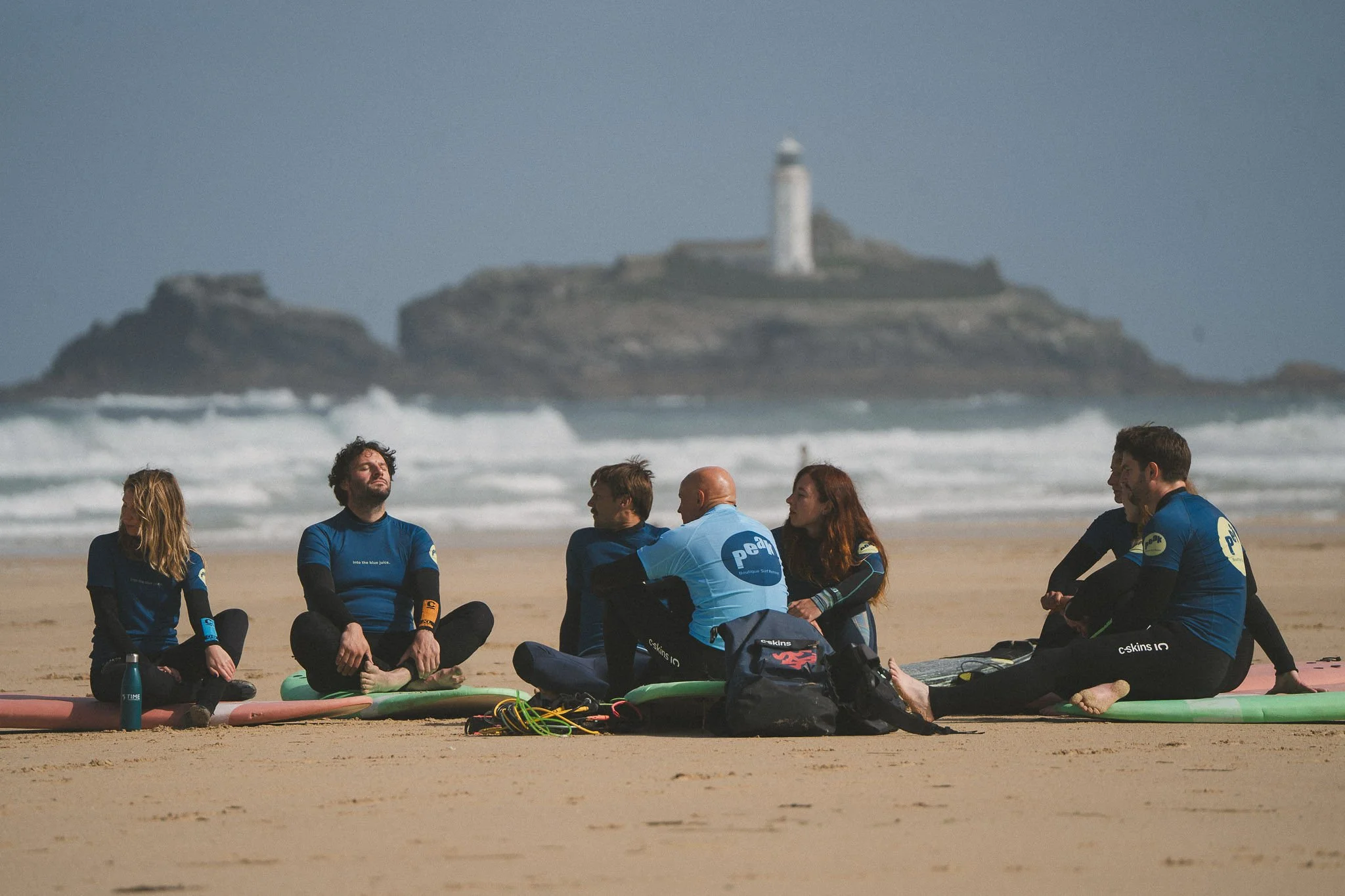 Small group of surfers with boards on a Cornwall beach, by the Godrevy lighthouse.