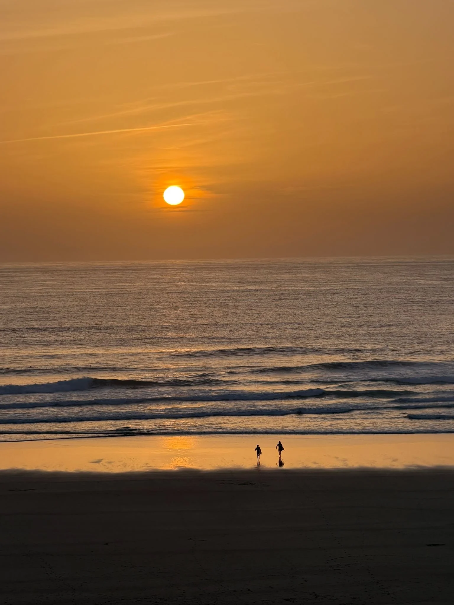 two guests at Peak surf retreat running into the sunset surf at Gwithian, in Cornwall.