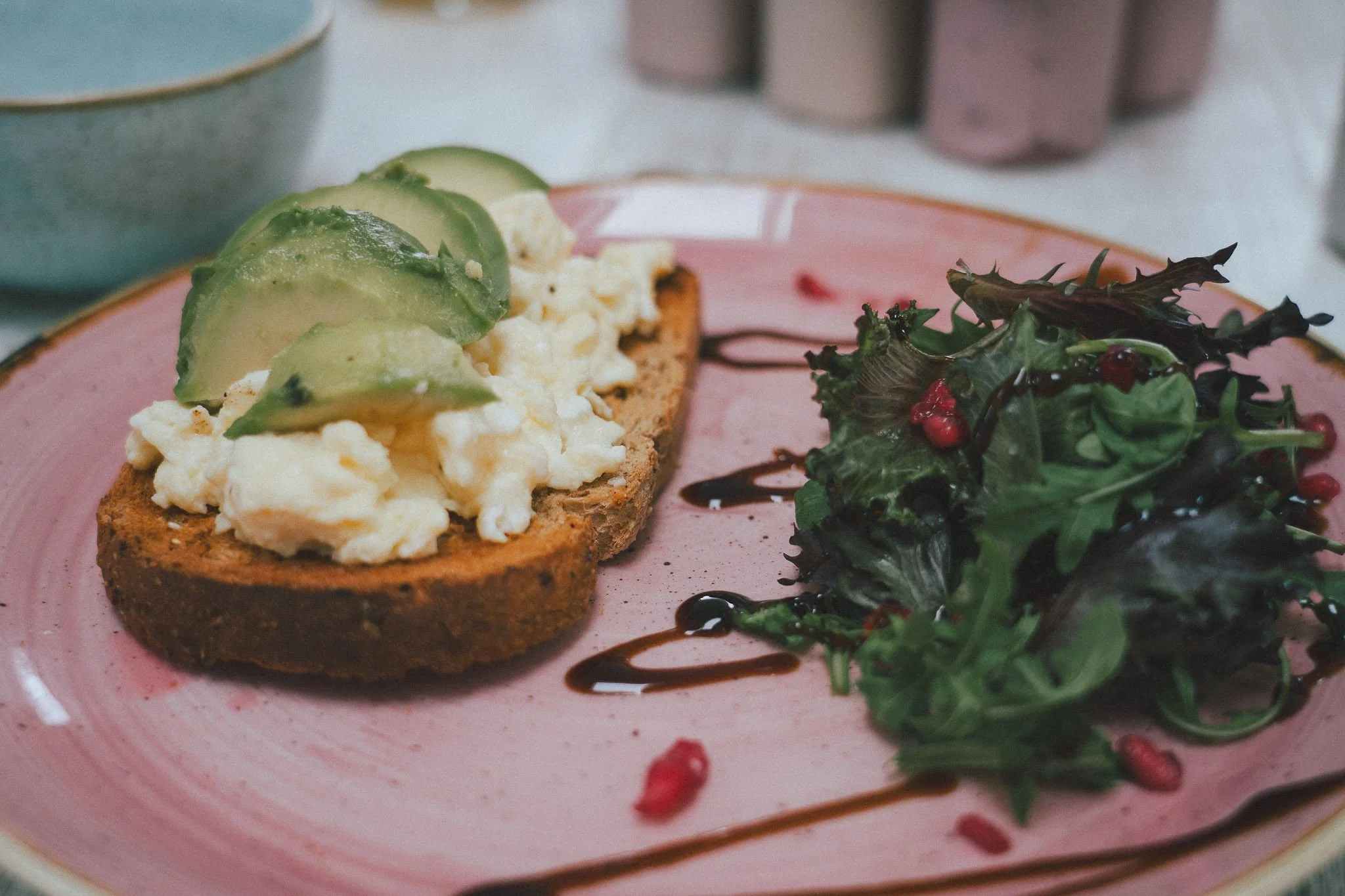 avocado and scrambled egg, with fresh side salad, on sourdough, on a breakfast table.