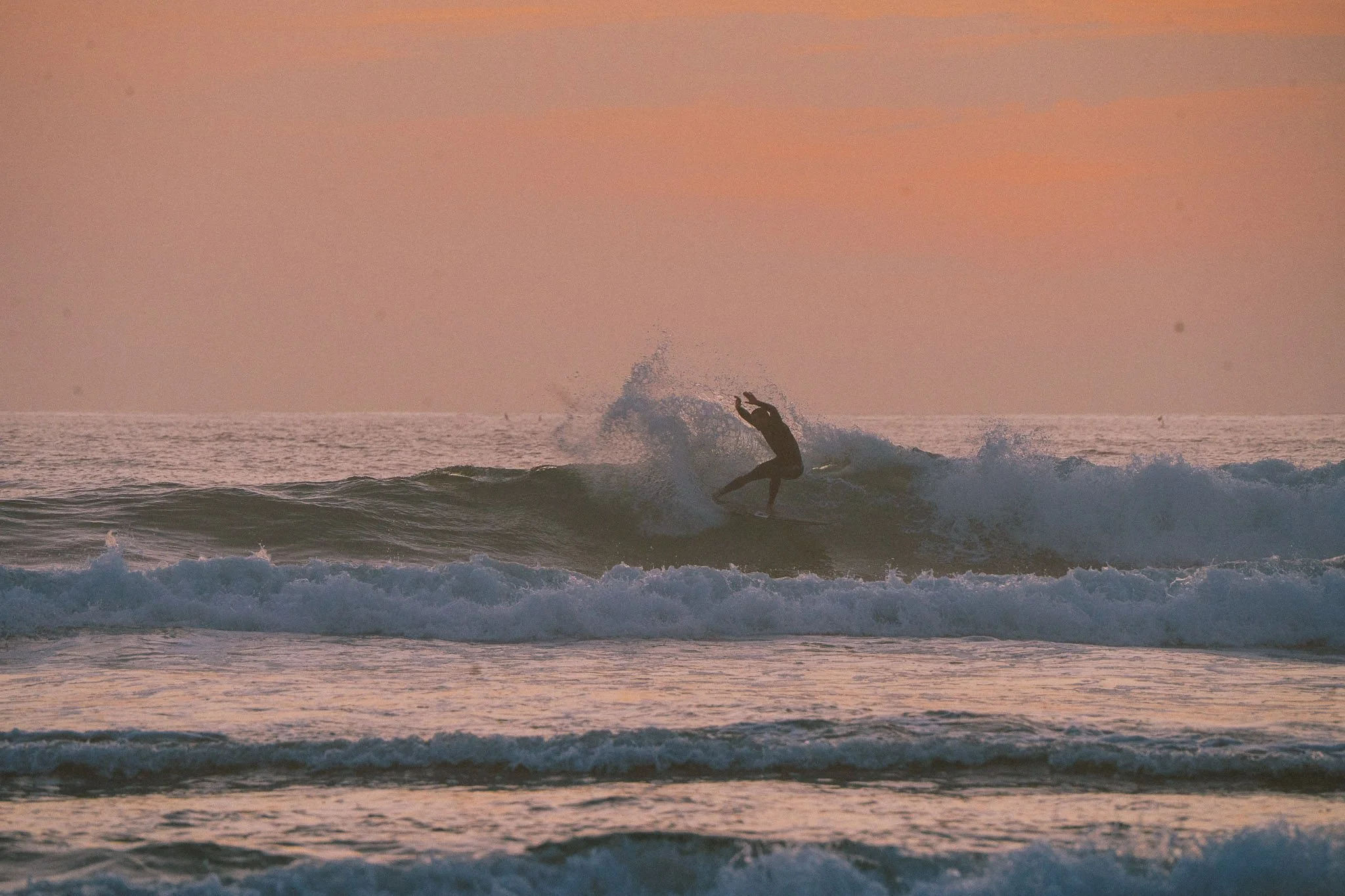 surfer getting spray off the lip during a sunset surf at Peak surf retreat in Gwithian, Cornwall.