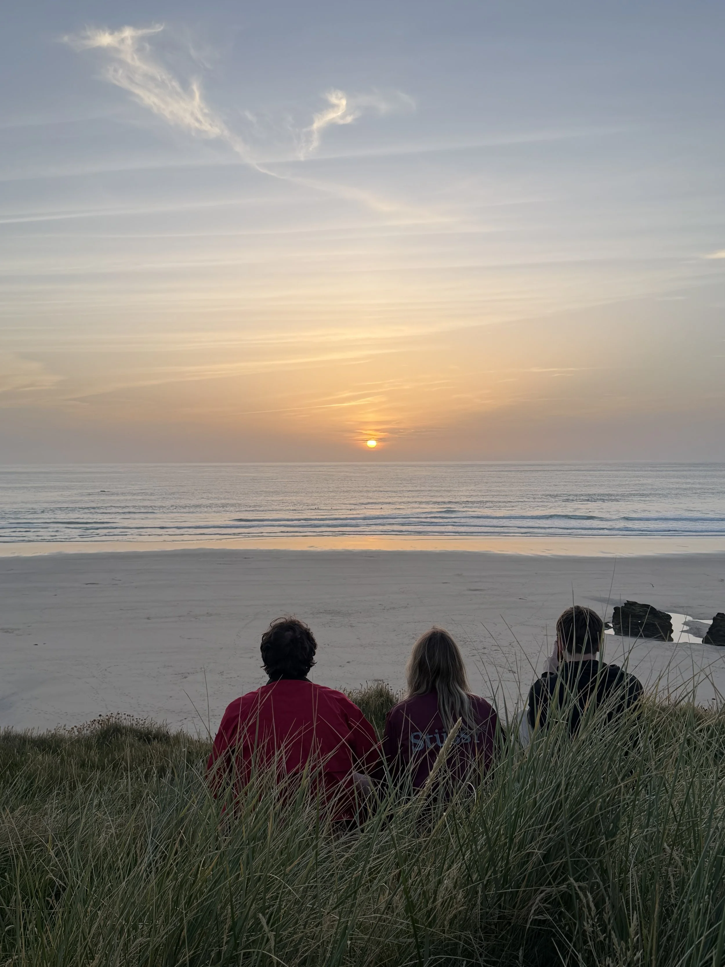 Three people watching the sunset over the Cornish coast during a digital detox