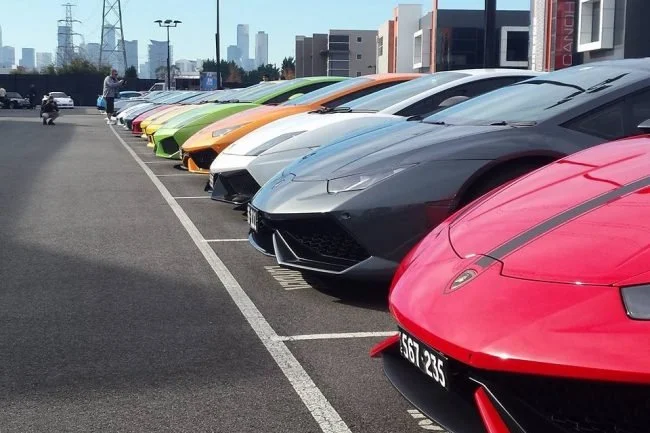 Row of colourful supercars with city skyline behind at Cannonball Run Australia