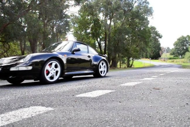 Black Porsche 911 Targa parked on a tree-lined road during the rally