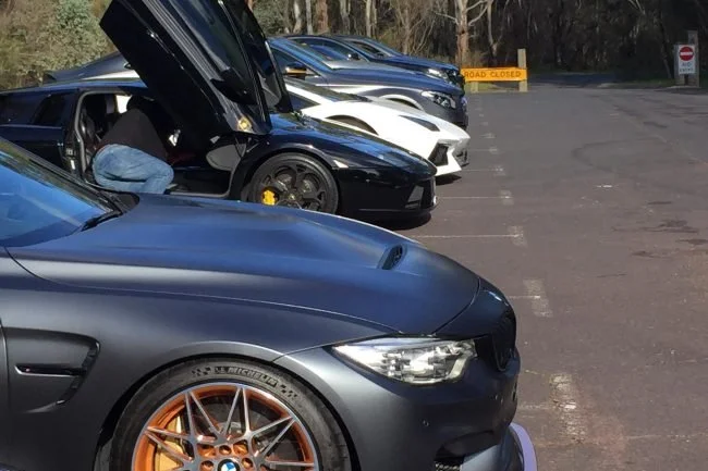 Black BMW M4 and a supercar with doors up at a rally stop