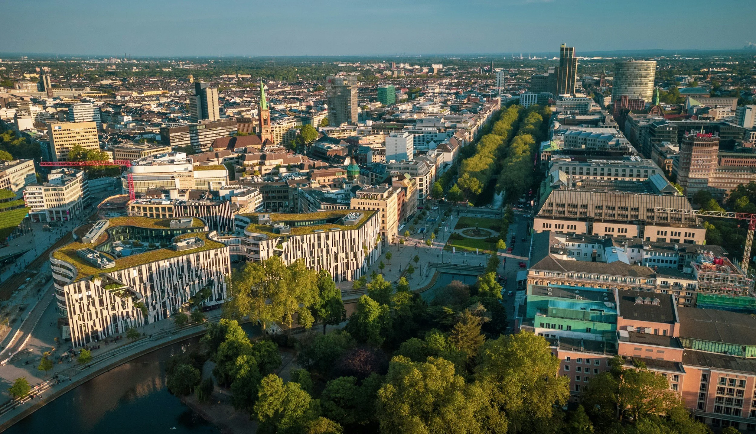 Luftaufnahme einer modernen Stadt mit hohen Gebäuden, Parks und Fluss, bei Sonnenuntergang.