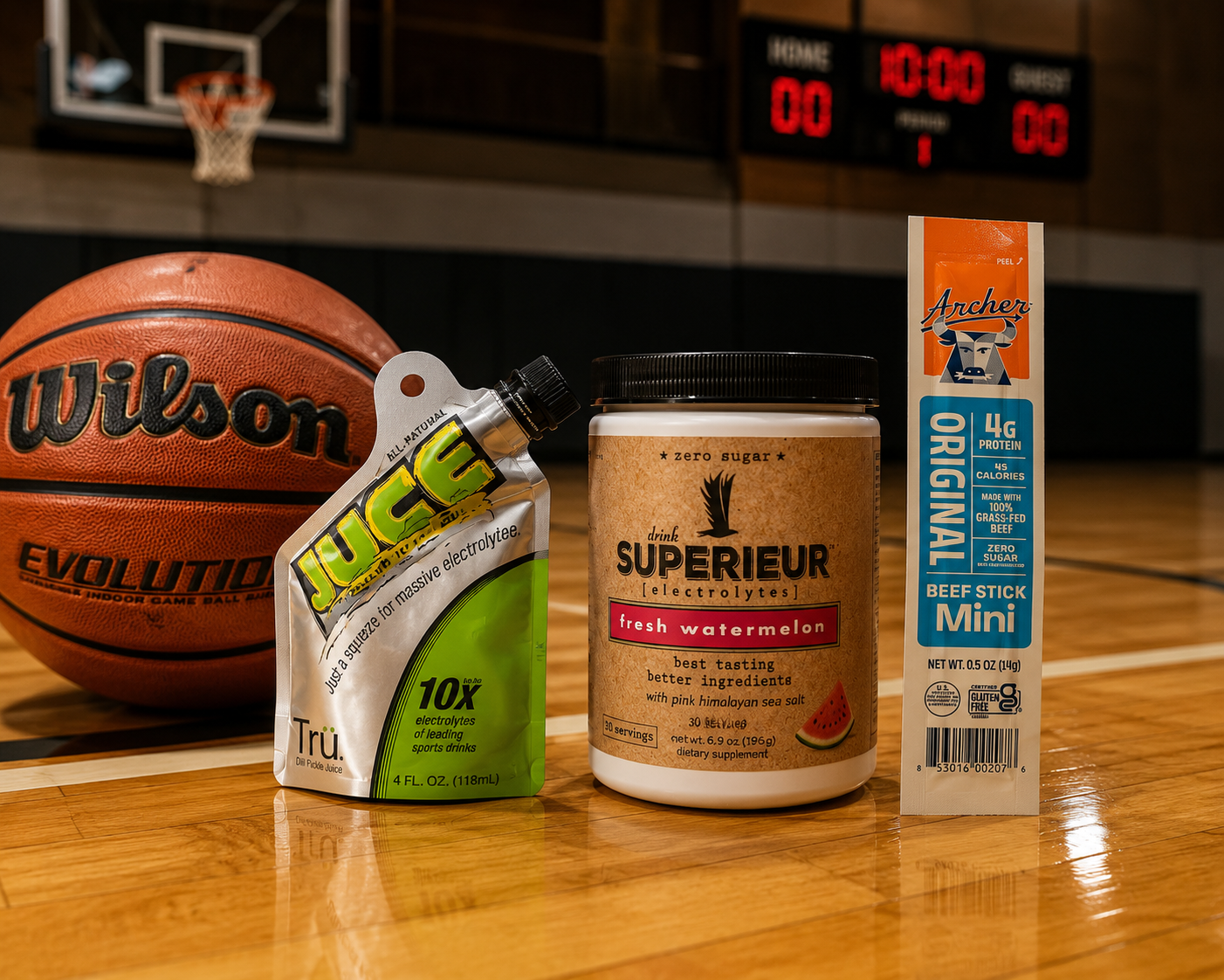 Basketball on a gym floor with electrolyte drinks, watermelon-flavored supplement, and beef jerky in front. Basketball has 'Wilson' written on it, with a scoreboard in background showing 10:00 and 00-00 scores.