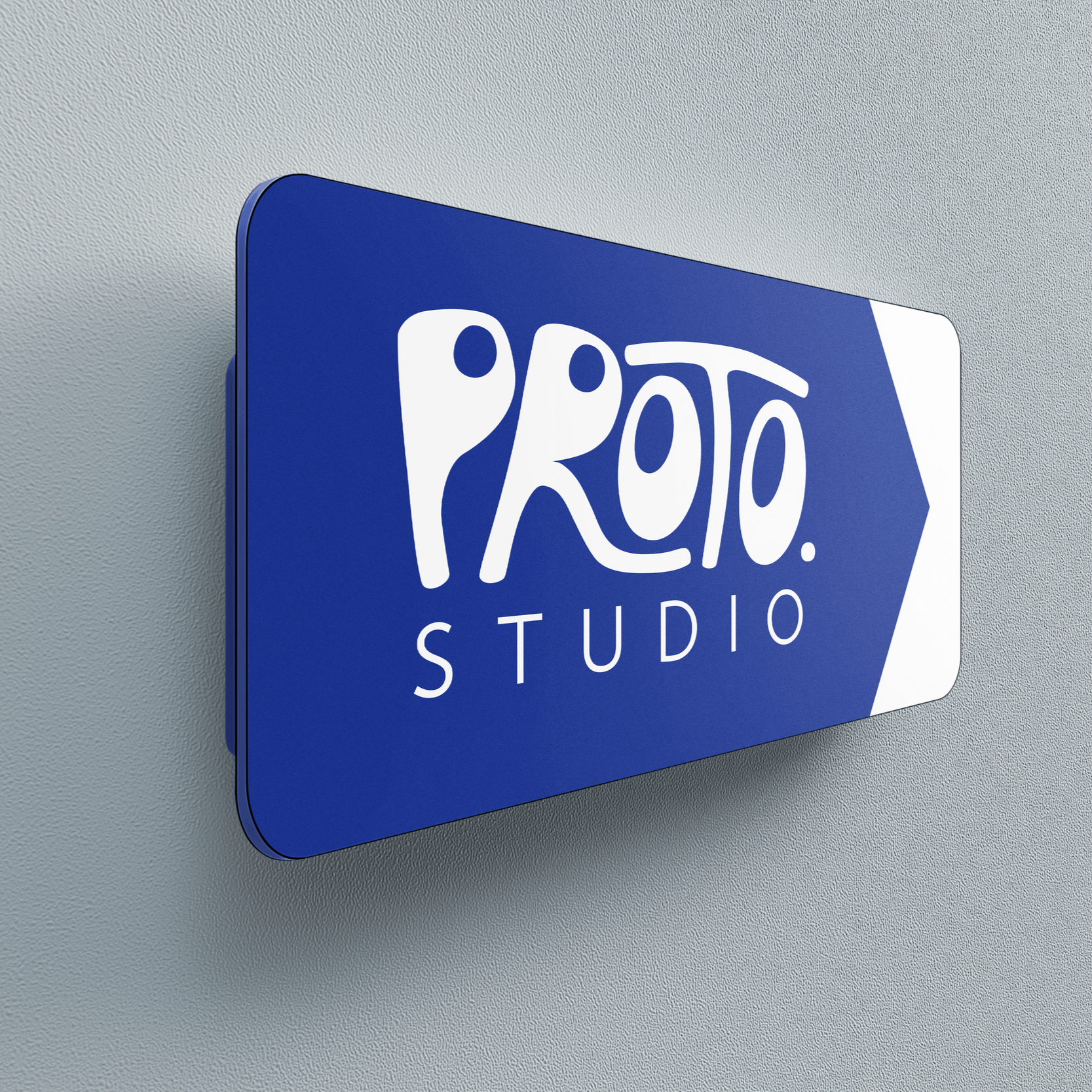 Blue rectangular sign with rounded corners reading "Proto. Studio" in white letters, mounted on a light gray textured wall.