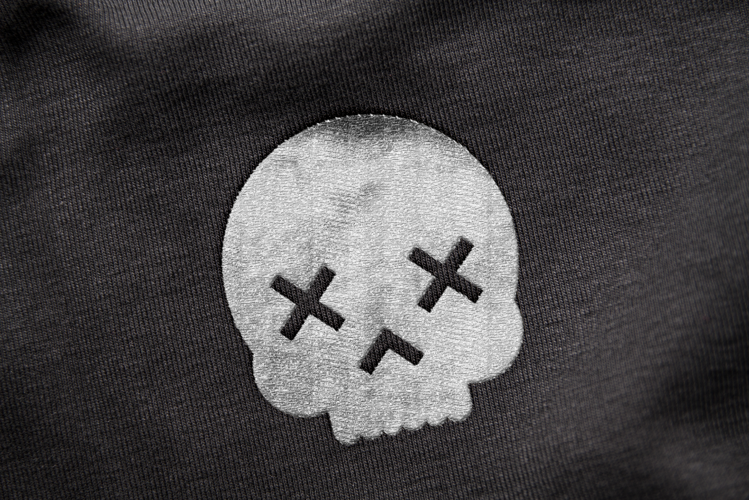 Close-up of a fabric patch of a skull with X's for eyes on a dark textured background.