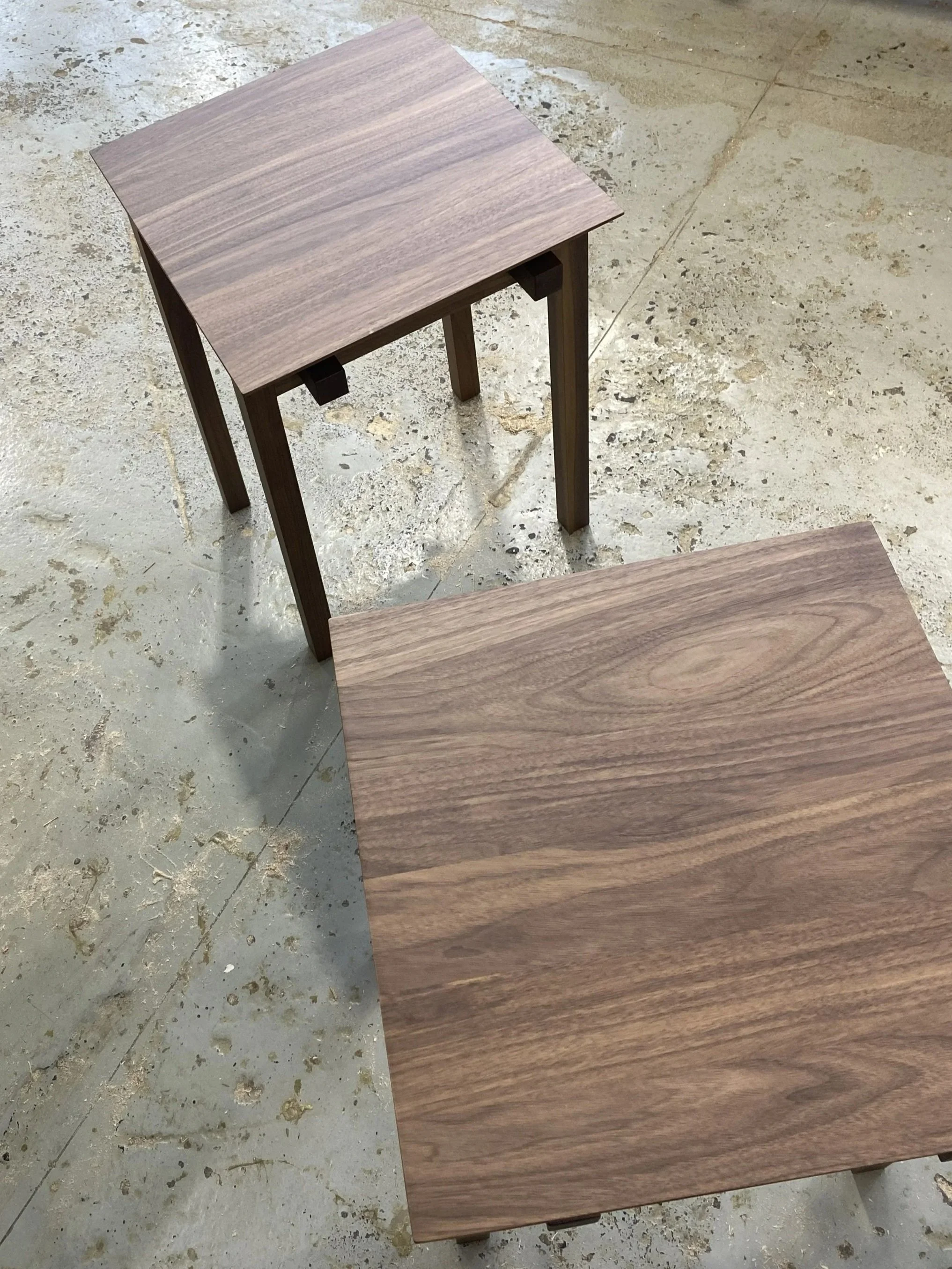 Two wooden tables with a natural wood finish placed on a concrete floor.