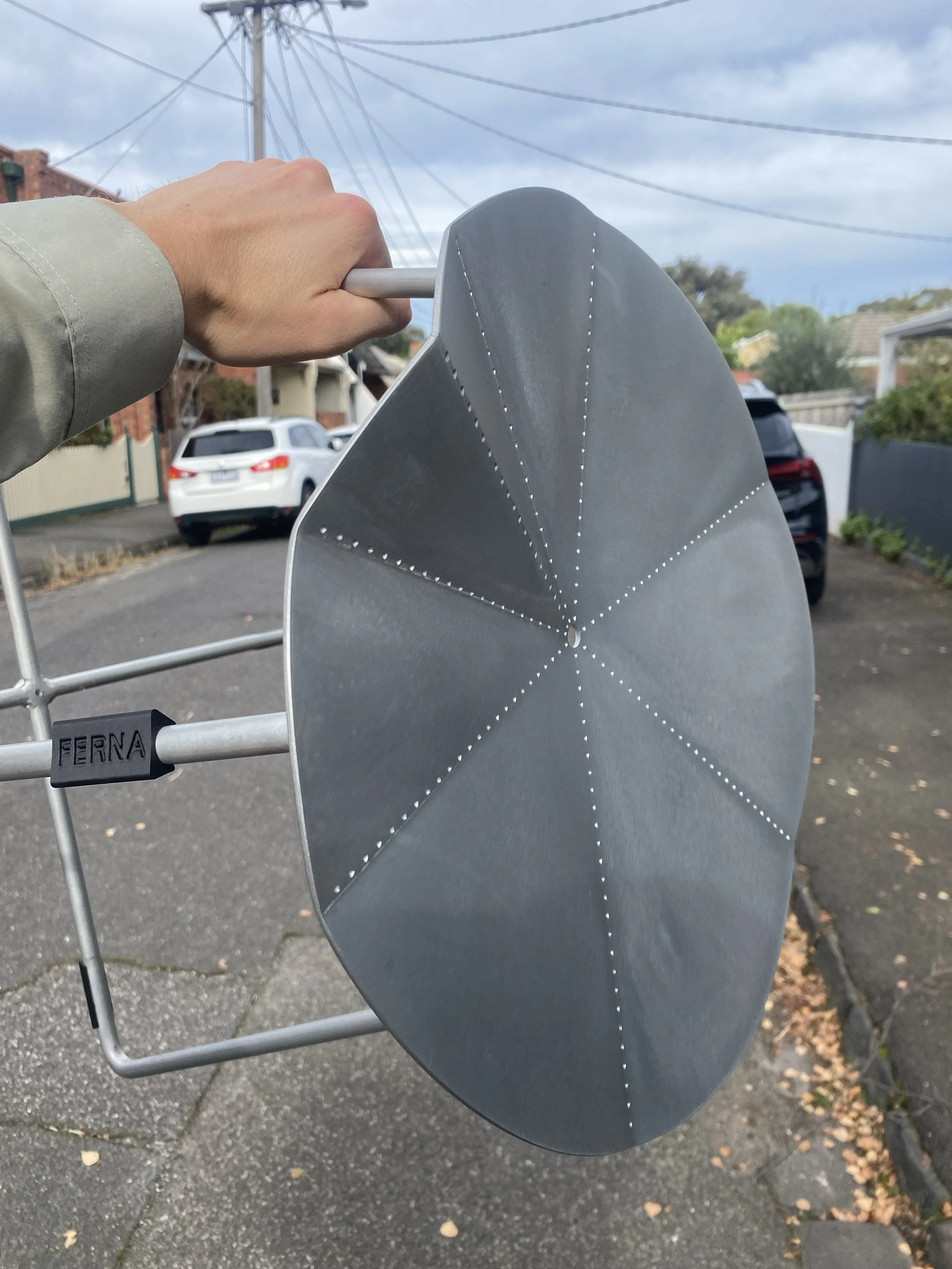 Close-up of a hand gripping a pole on a satellite dish with a suburban street and parked cars in the background.