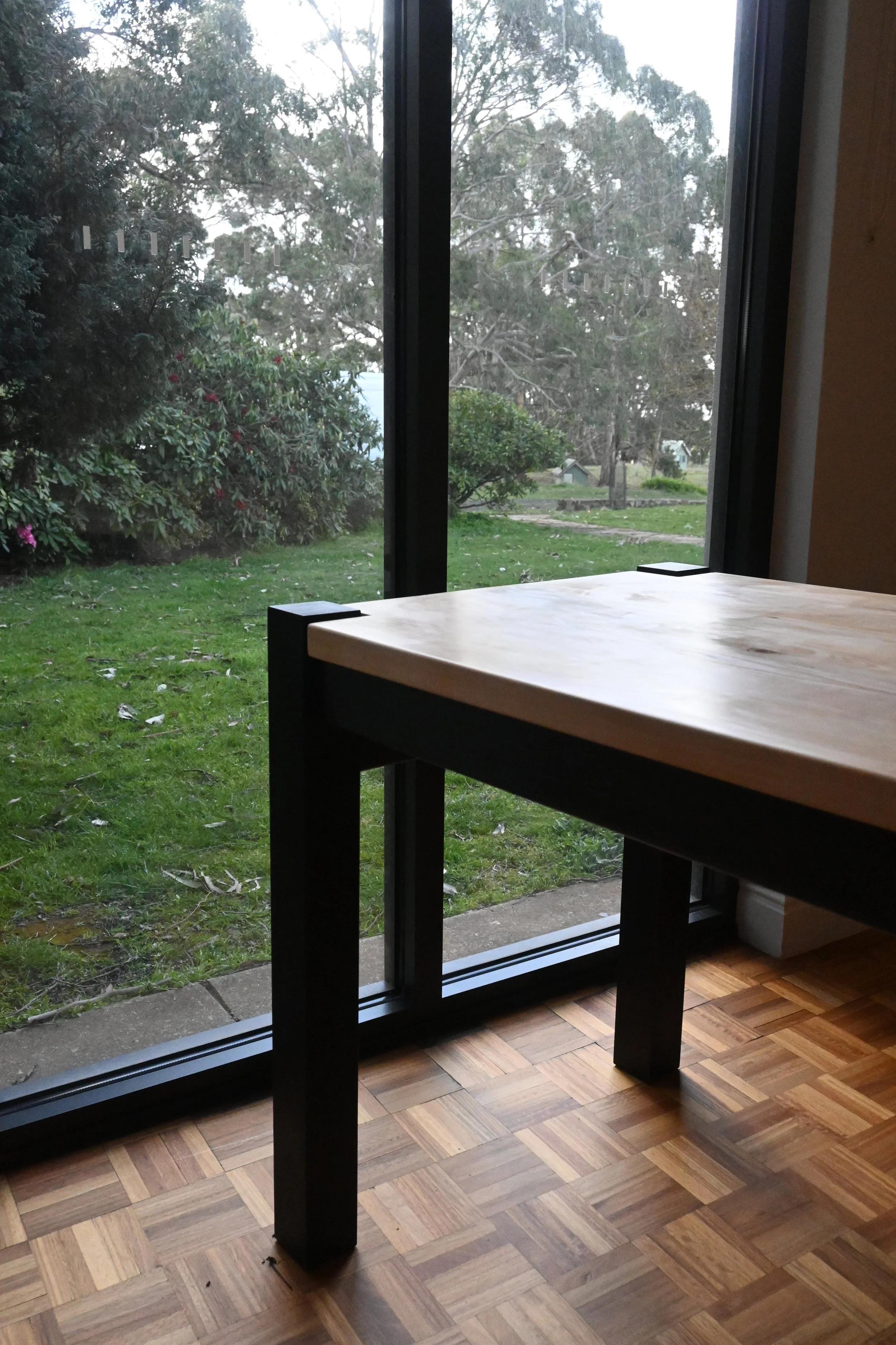 View from inside a room looking out through a glass sliding door onto a backyard with green grass, bushes, trees, and a small shed.