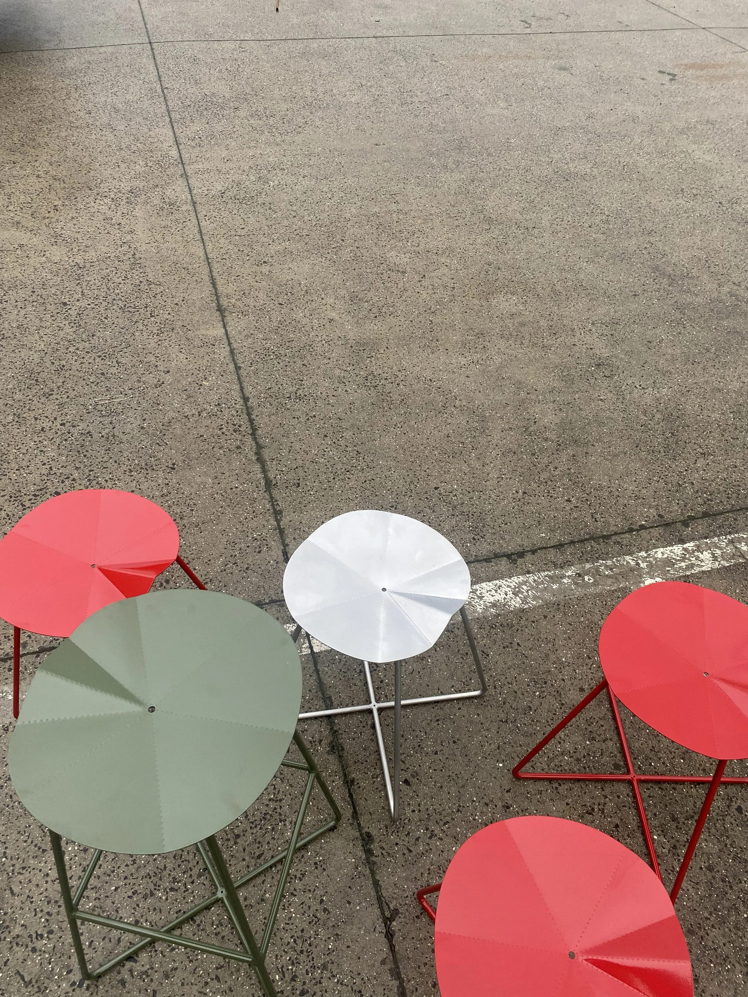 Multiple round tables with umbrellas in red, white, and pale green on a concrete sidewalk.