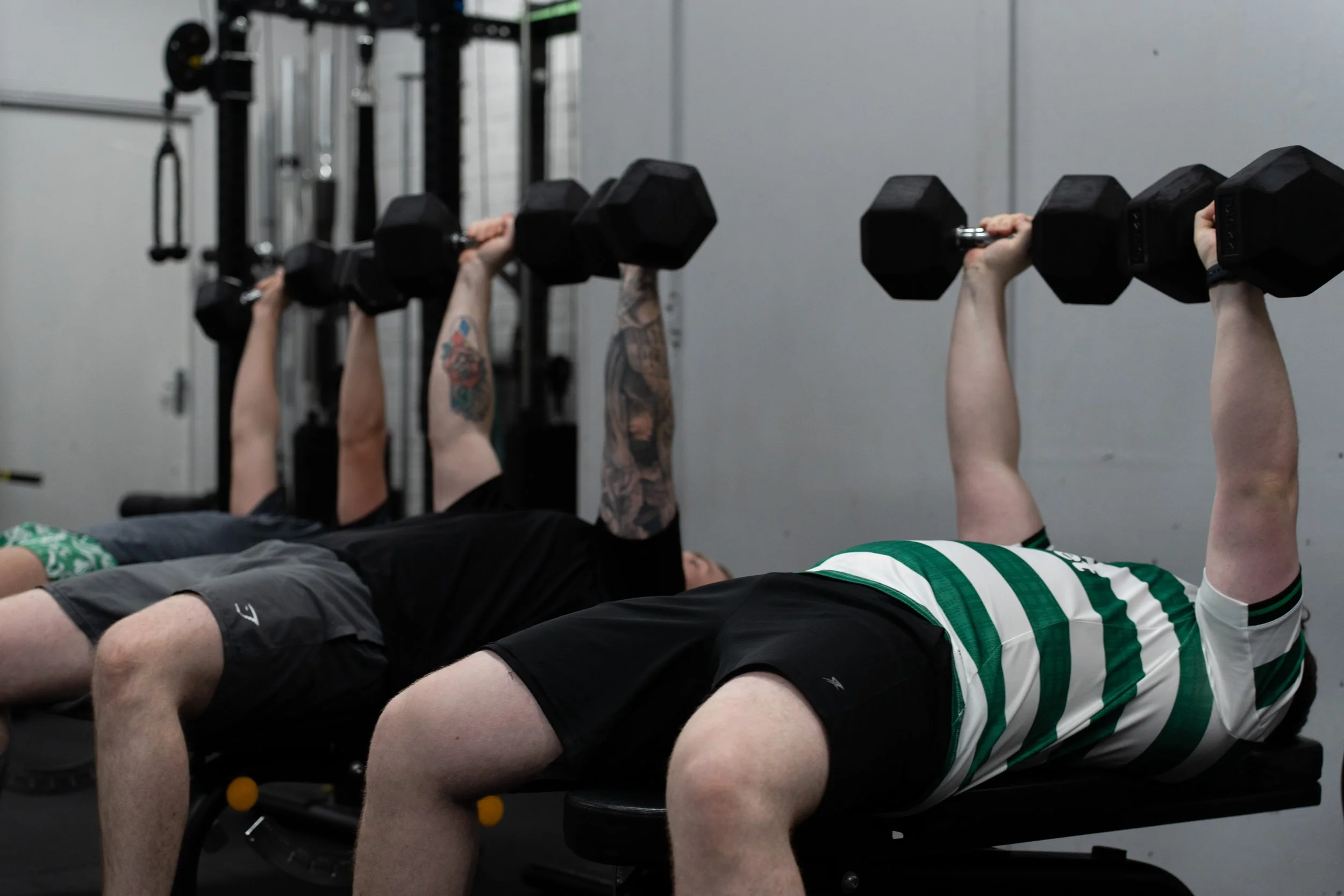 People lying on exercise benches lifting dumbbells in a gym.