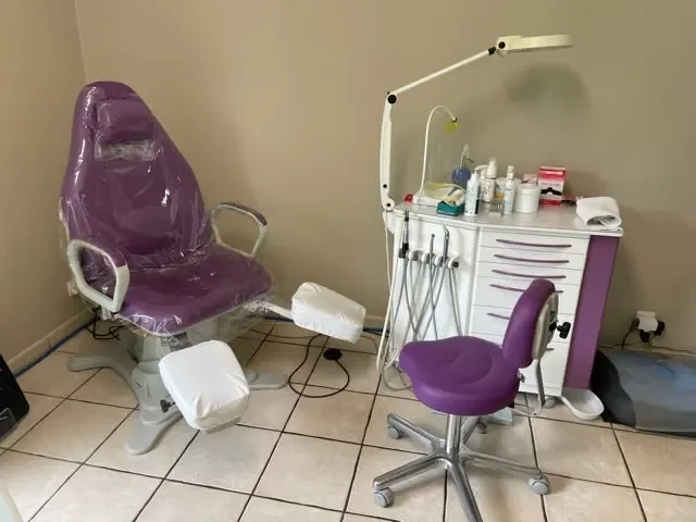 Salle d'examen pédicure-podologue avec fauteuil violet, équipement dentaire sur un meuble blanc, et chaise de bureau violette.