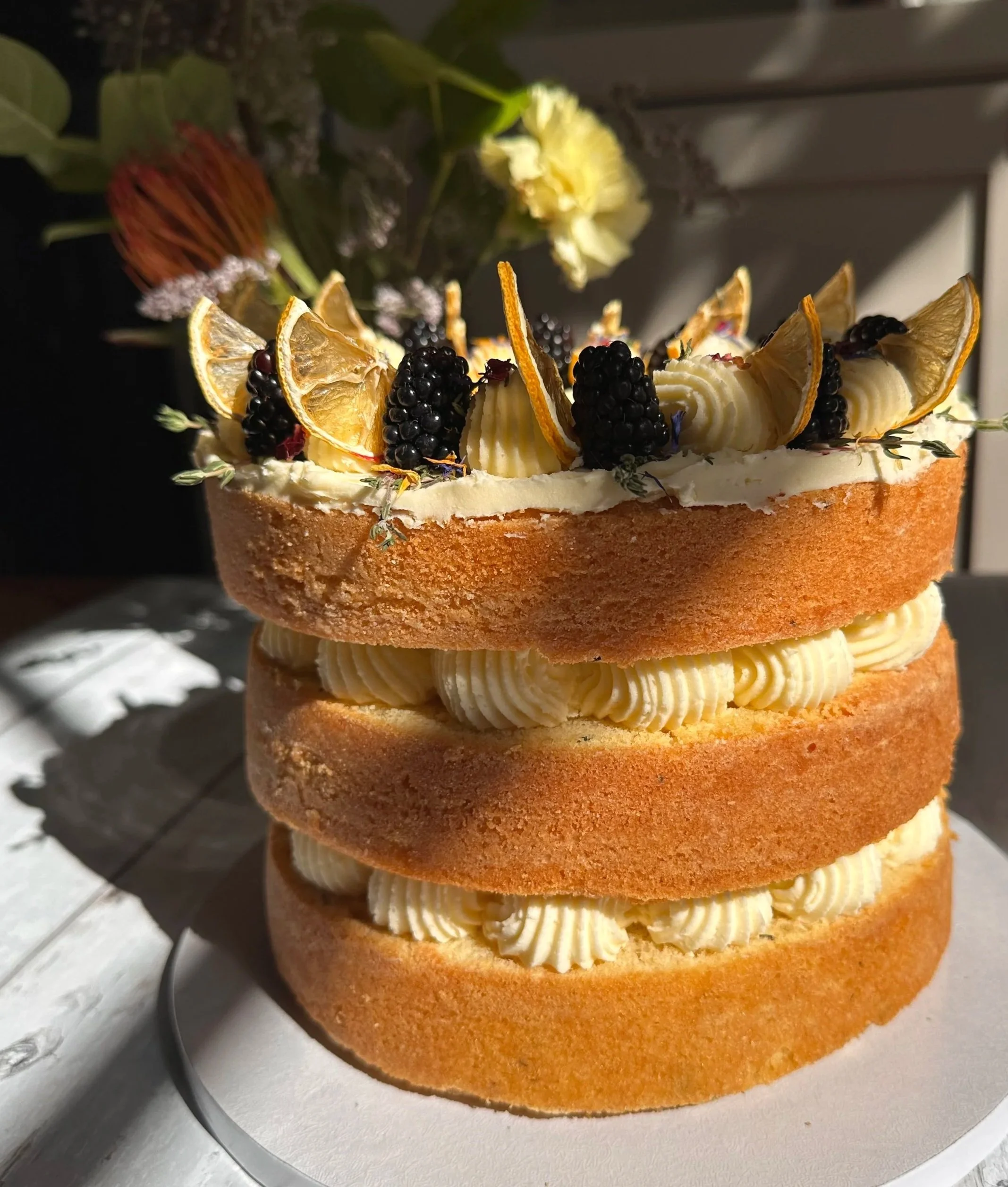 Triple-layered celebration cake decorated with dried orange slices, blackberries, and cream swirls.