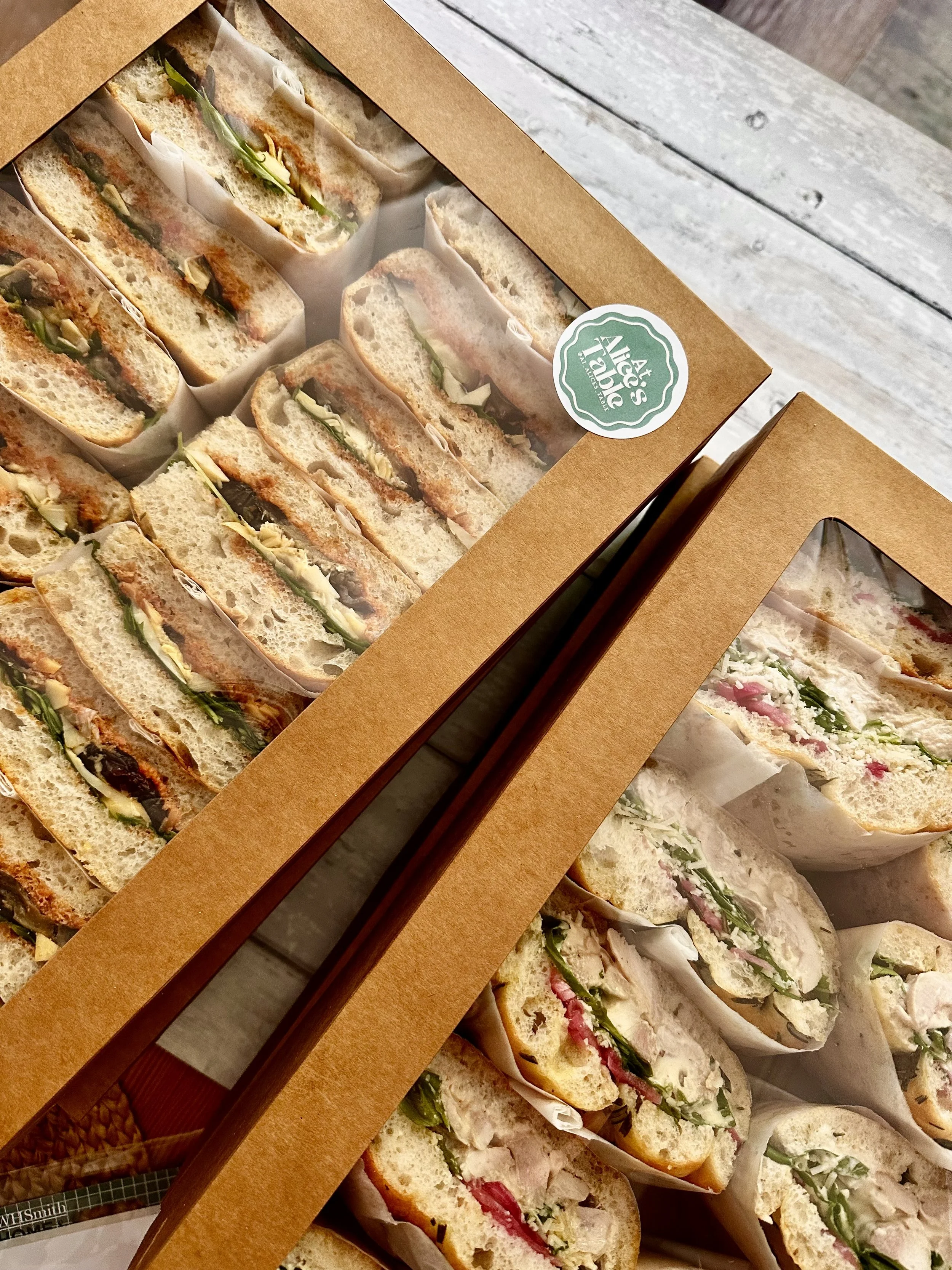 A selection of sandwiches in a cardboard box with a window, filled with various ingredients including vegetables, meats, and cheeses.