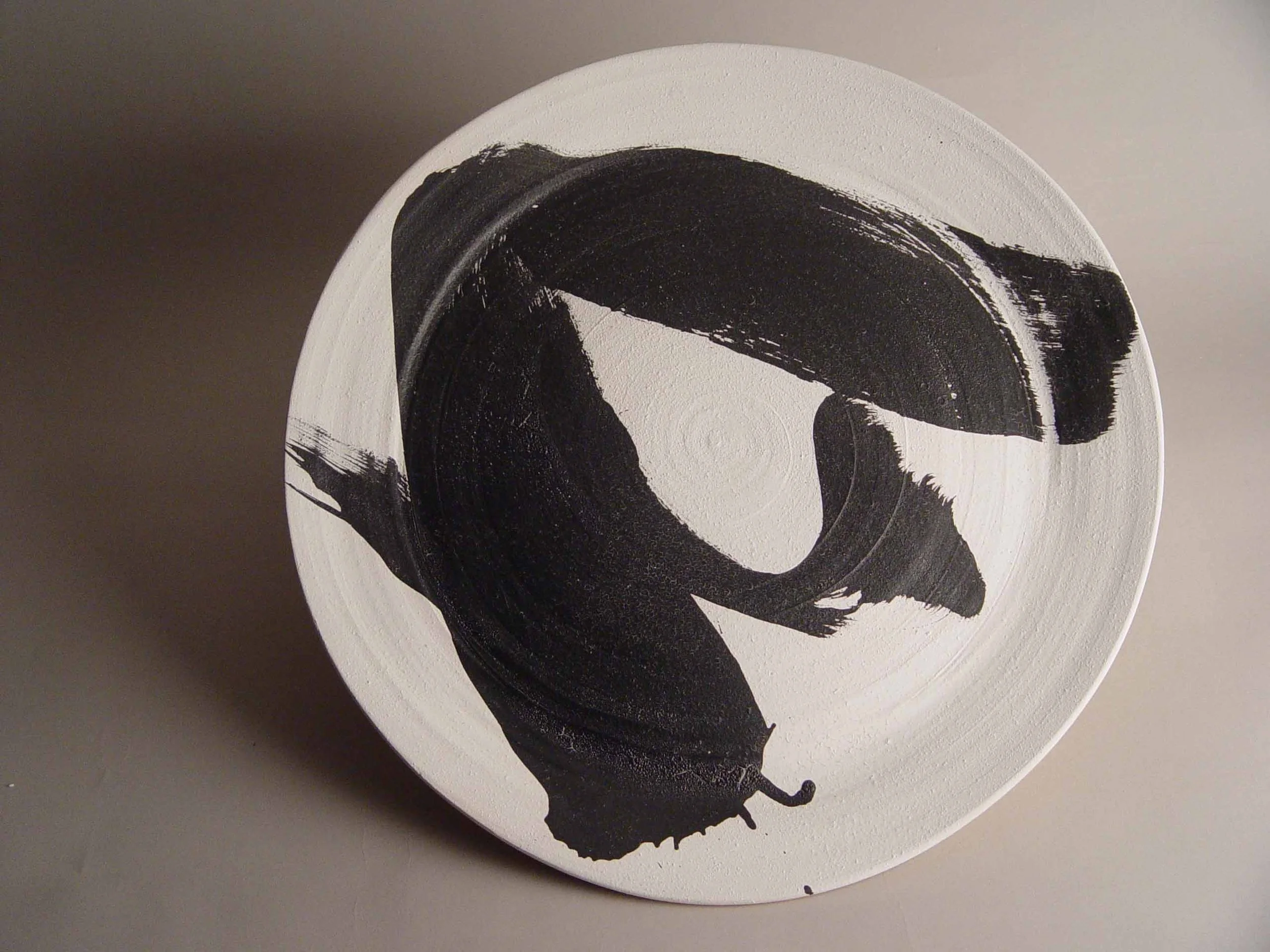 Abstract black brushstroke on a white circular surface.