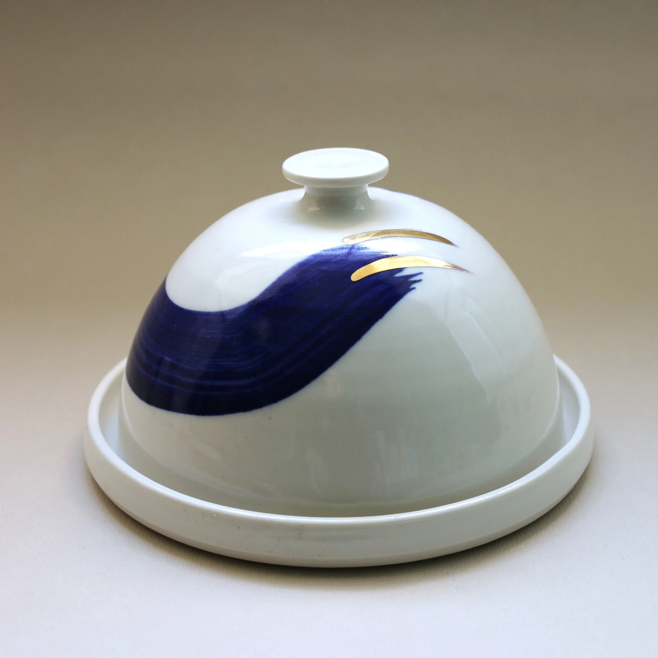 Close-up image of a white ceramic tea pot with a lid, decorated with blue and gold patterns, placed on a flat surface.