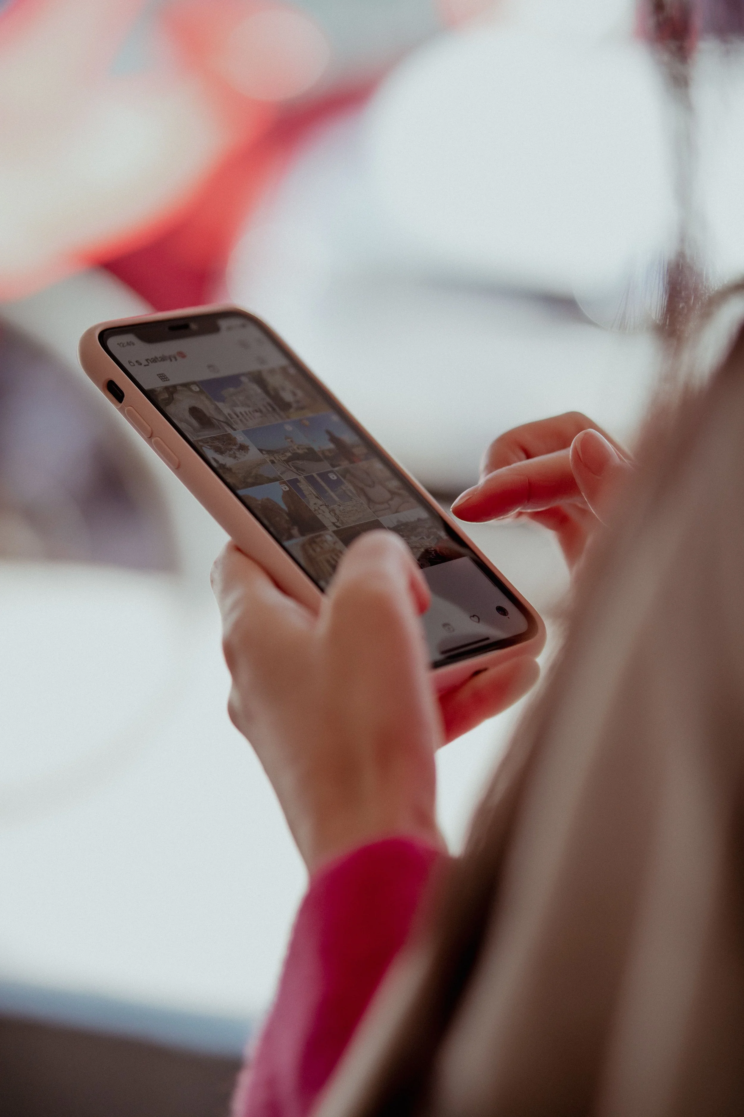 A person holding a smartphone showing a photo gallery on the screen, with a light-colored background.