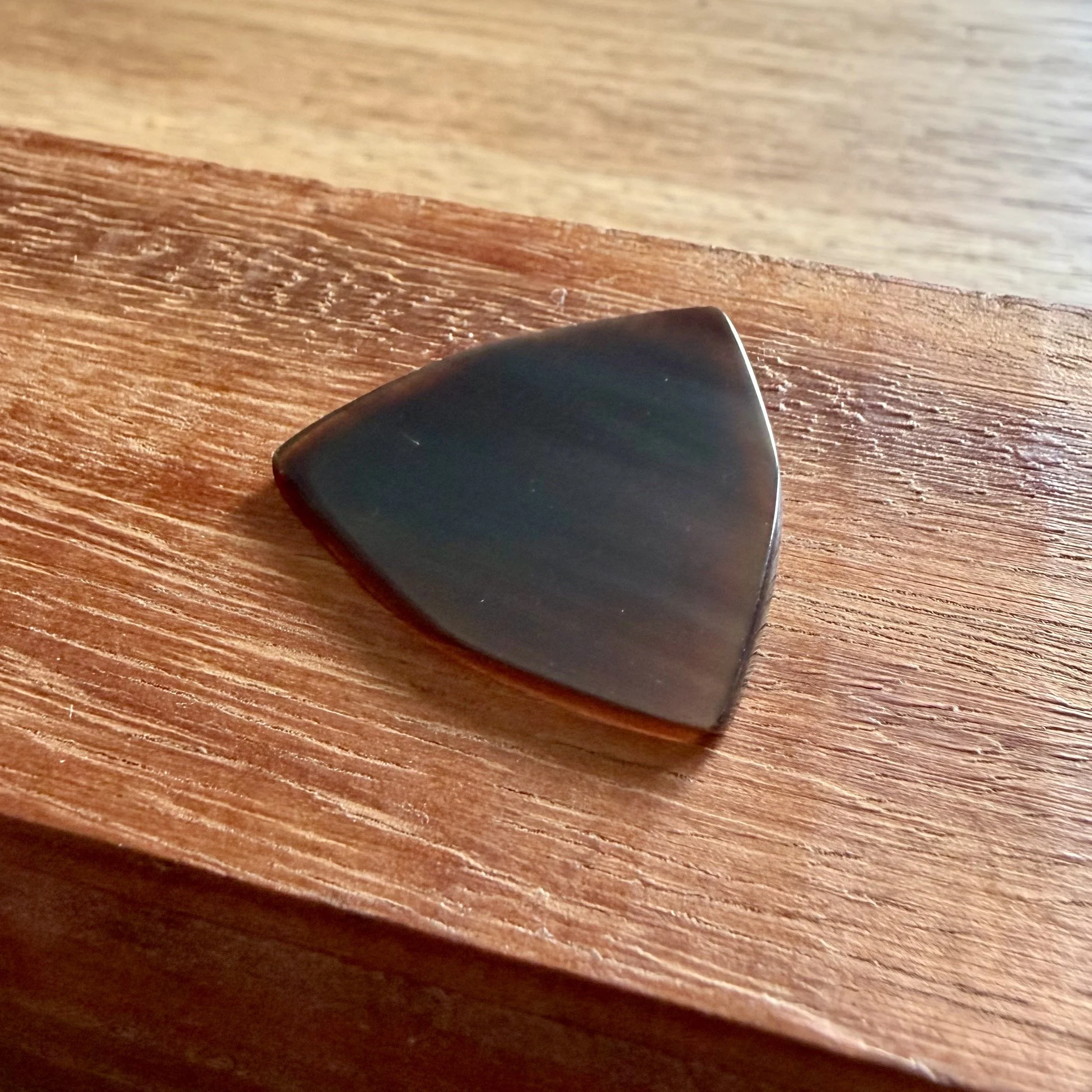 Close-up of a black guitar pick resting on a wooden surface.
