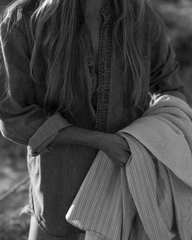 A person with long hair wearing a denim jacket, partially visible, holding a striped fabric or clothing item.