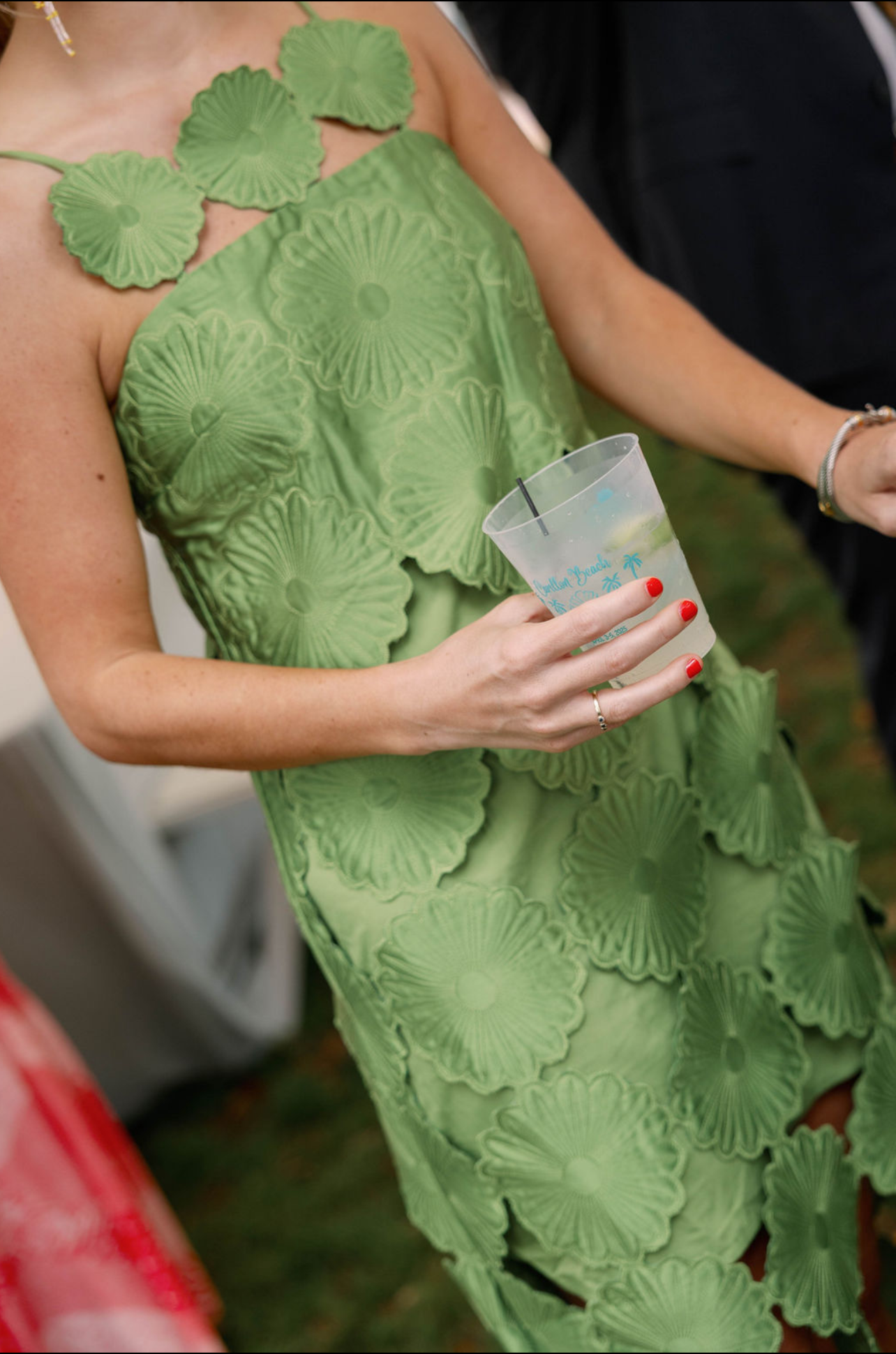 A woman in a green dress with a floral pattern, holding a clear plastic cup with a drink and straw.