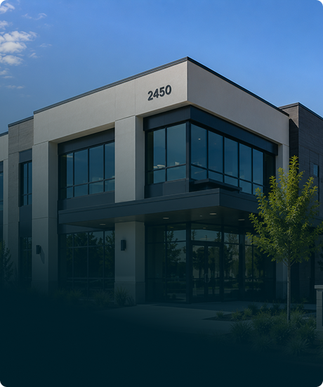 Modern two-story commercial building with large glass windows, white exterior walls, and the number 2450 on top, surrounded by landscaping and a small tree.