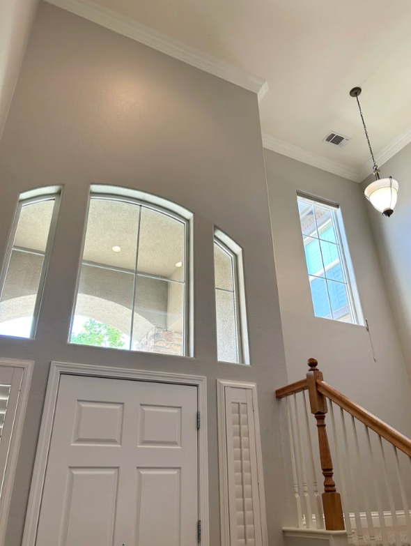 Interior view of a two-story foyer with high ceilings, a chandelier, and large windows near the staircase.