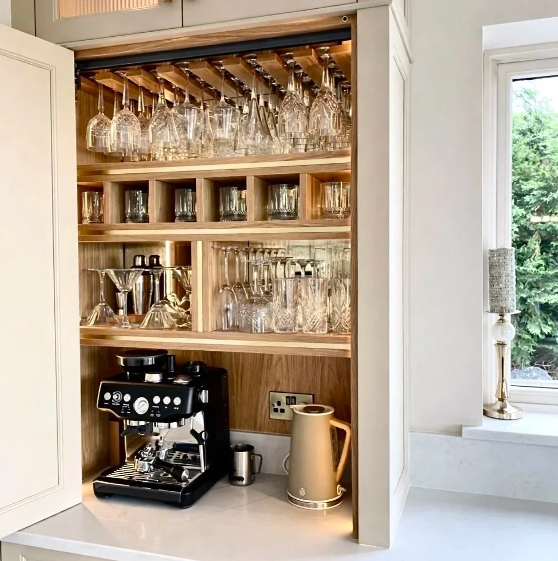 Kitchen cabinet with glassware and a coffee machine on the countertop near a window.