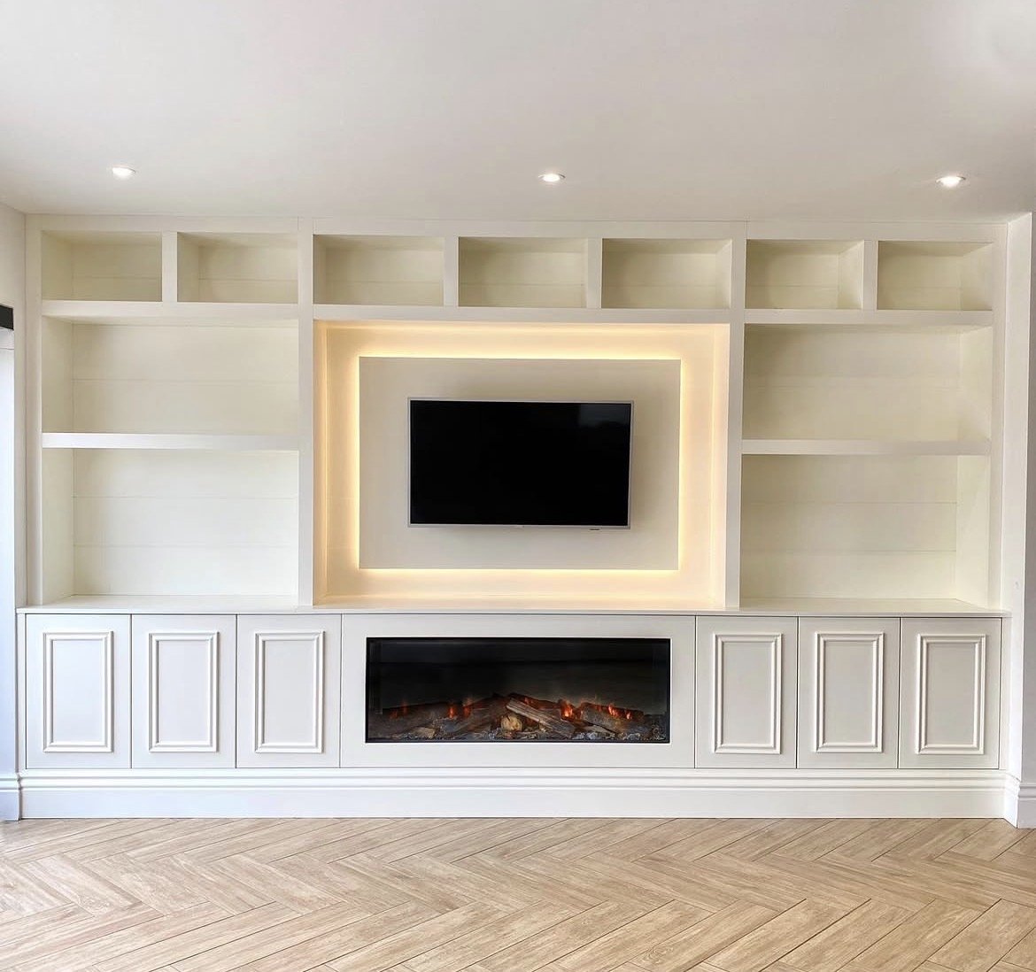 Modern white entertainment center with a built-in electric fireplace and a mounted flat-screen TV, featuring open shelves and cabinet doors, in a contemporary living room.