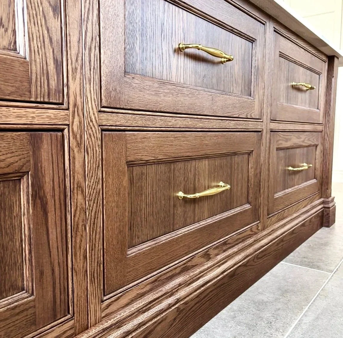 Close-up view of a wooden cabinet with multiple drawers and gold-colored handles, positioned on a tiled floor.