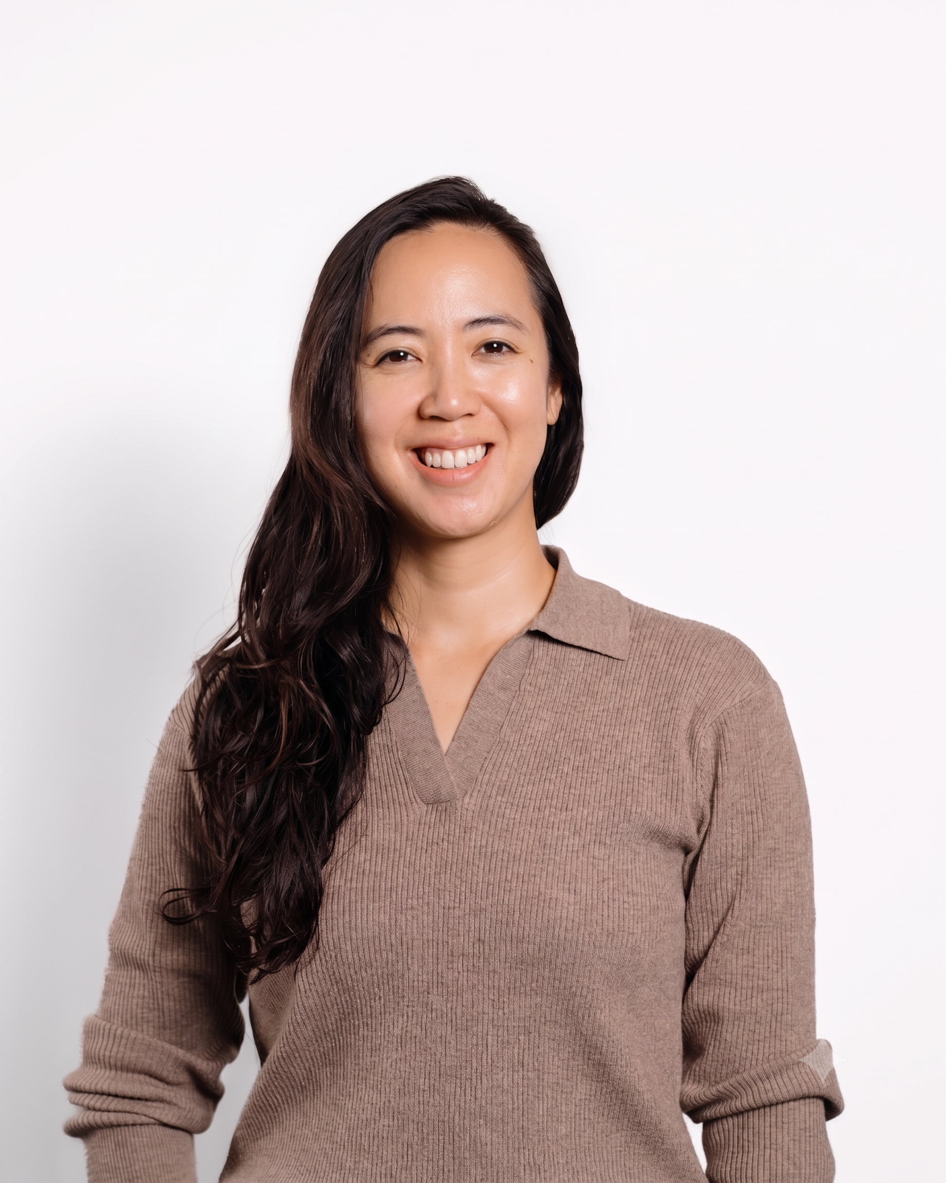 A woman with long dark hair smiling, wearing a beige V-neck sweater, against a white background.