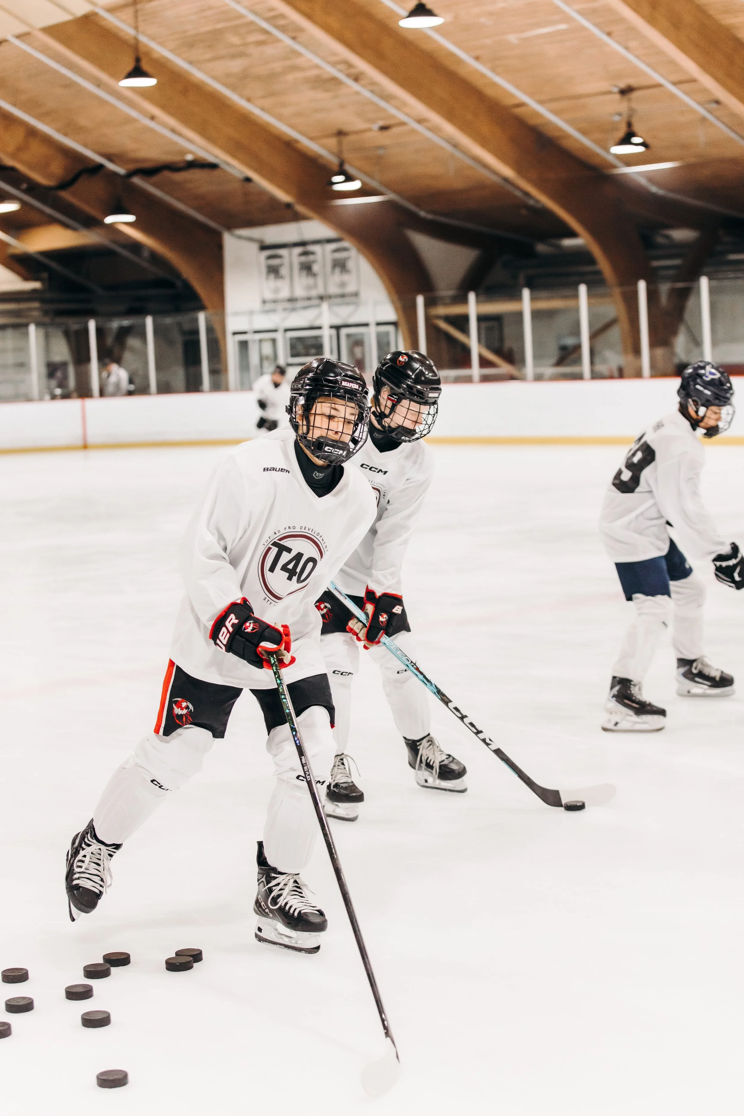 Hockey players in white jerseys practicing drills on an indoor ice rink.