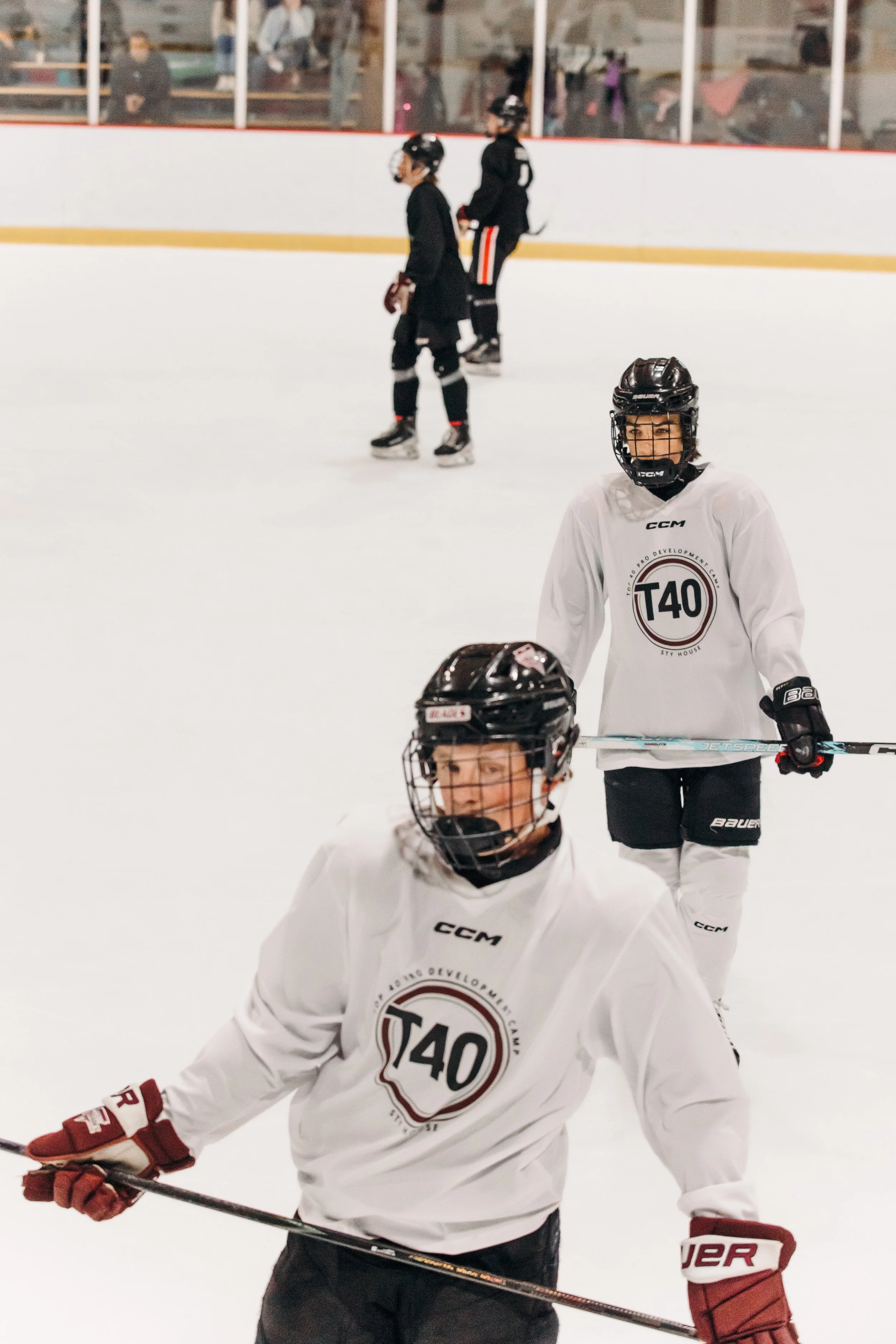 Kids in ice hockey gear on an ice rink, with some spectators visible behind the glass.