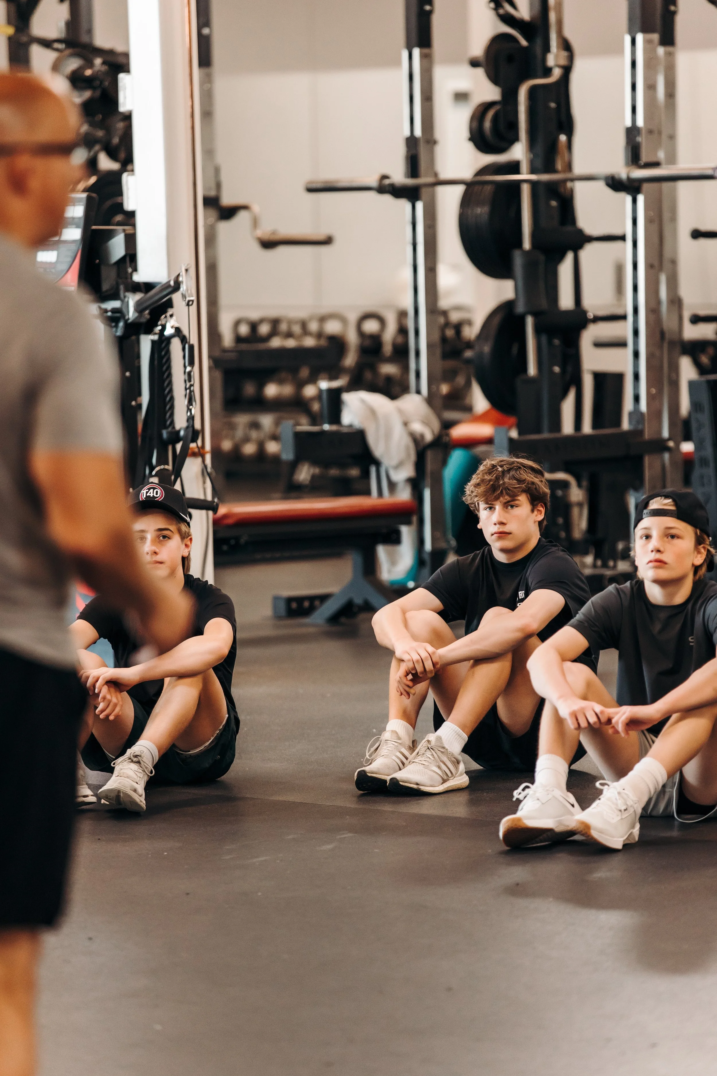 Group of young people sitting on the gym floor during a fitness class or training session at a gym.