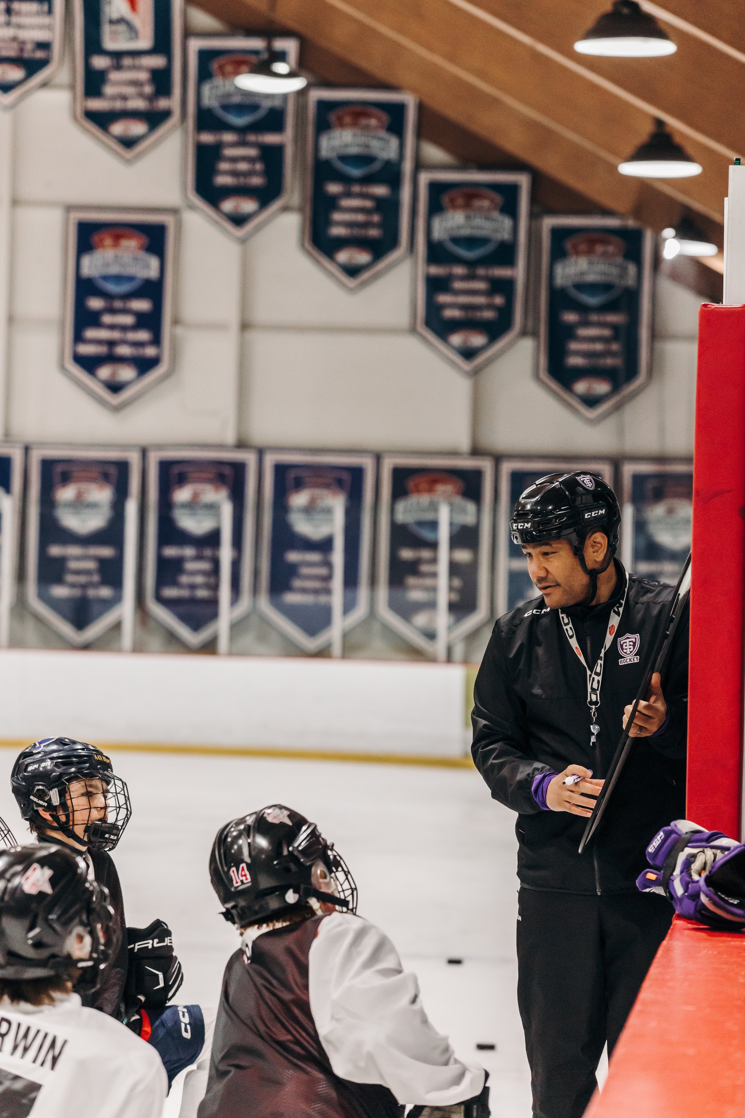 Hockey coach giving instructions to young players during a practice session in an indoor rink.
