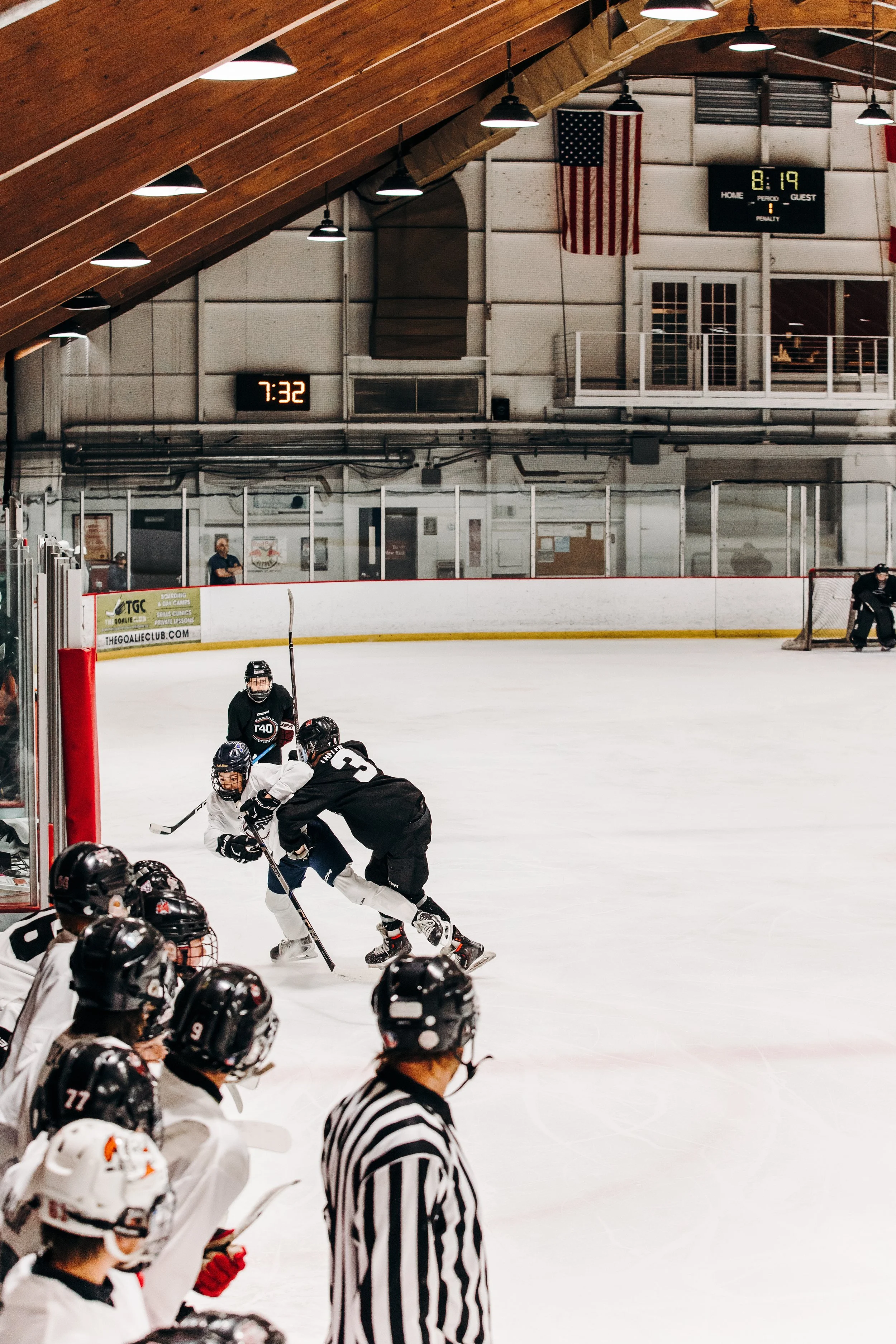 Hockey players on ice rink with referees, American flag, and scoreboard showing 8:19 in the background.