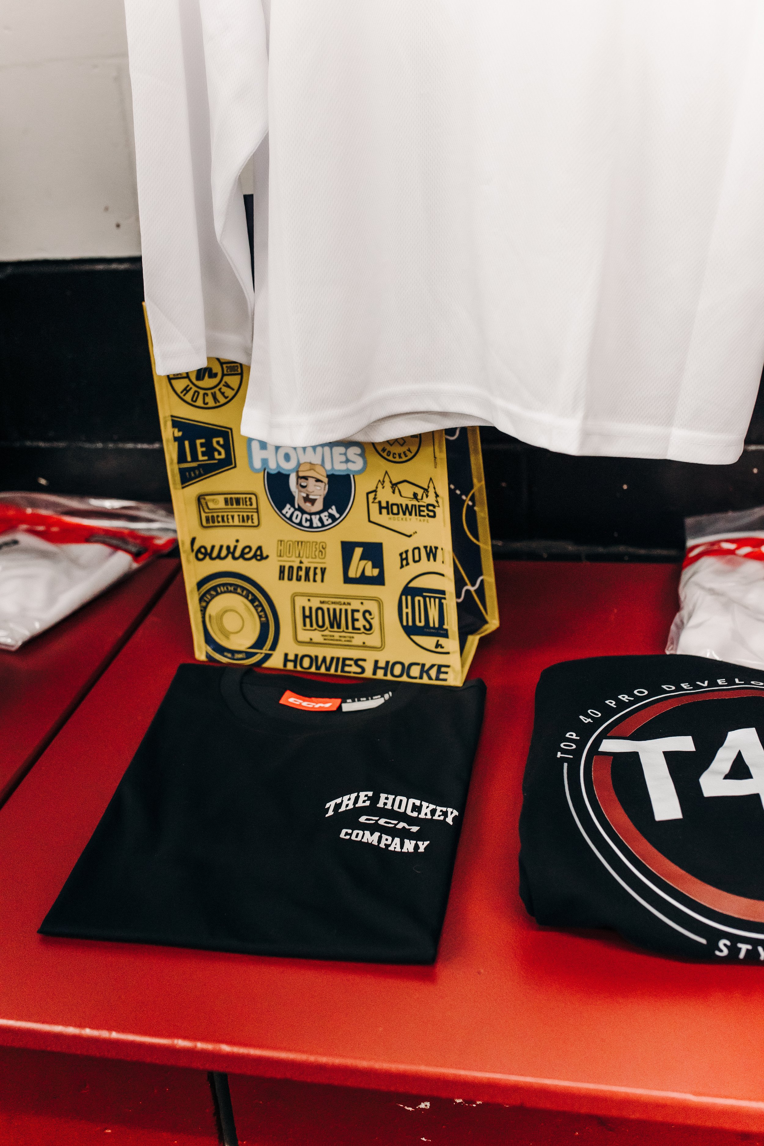 A white hockey jersey hanging above a box of hockey tape and hockey-related items on a red table.