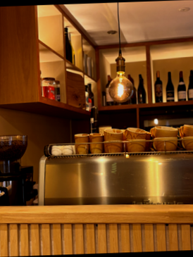Coffee shop counter with glass display case, cups, and hanging light bulb in a cozy cafe setting.