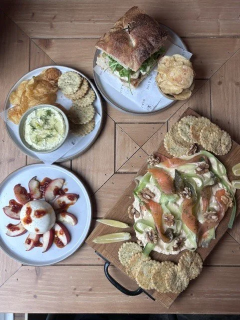 Spicy pizza with vegetables, served on a wooden board with chips and dips, along with a sandwich, side salad, and a soft-boiled egg with sauce on a white plate.