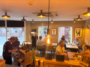 Interior of a lively cafe with customers sitting at tables, a person ordering at the counter, and sunlight coming through the windows, creating a warm atmosphere.
