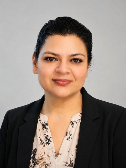 Professional portrait of a woman with dark hair, wearing a black blazer and a floral blouse, against a gray background.