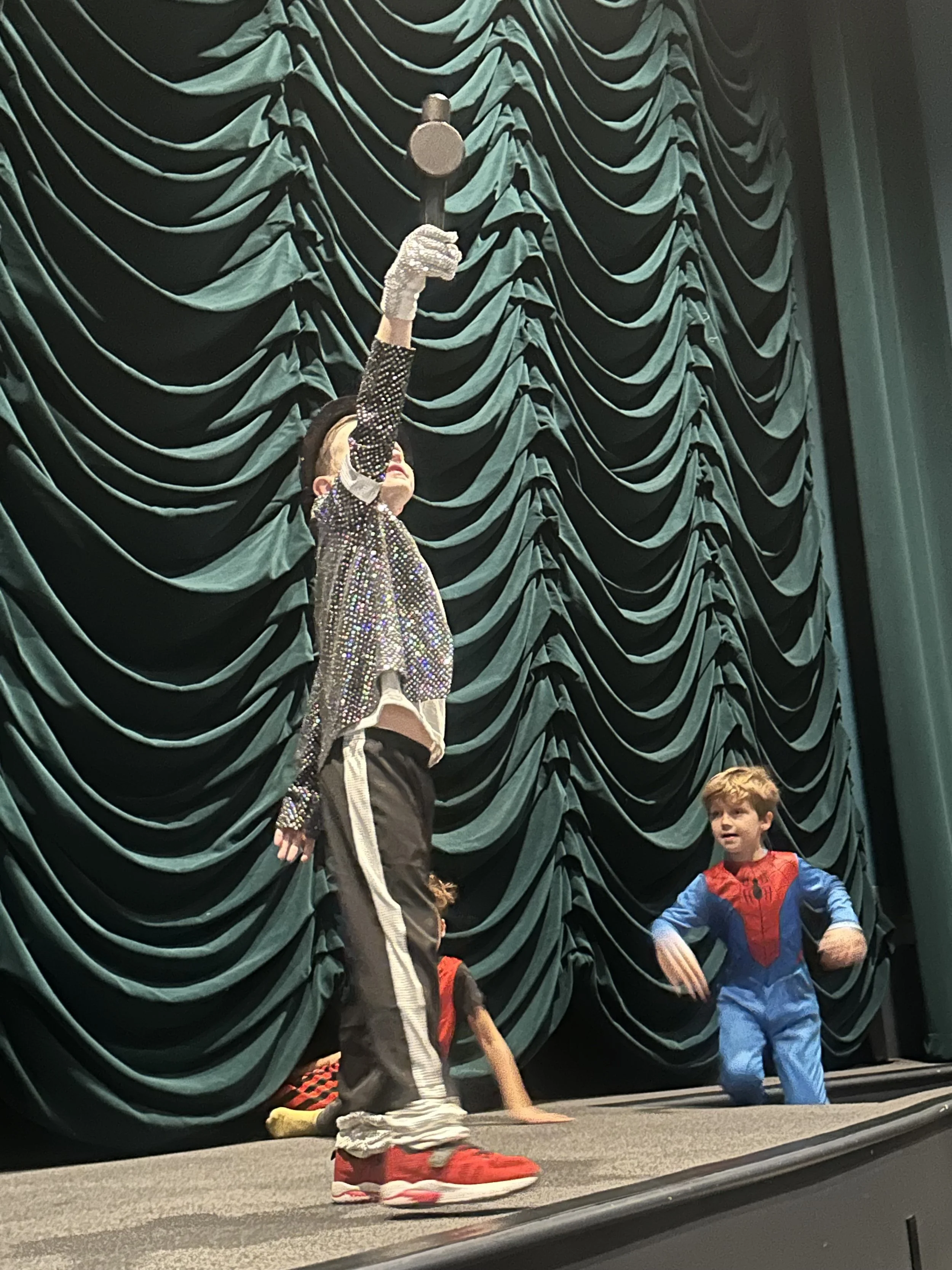 Children on stage dressed as superheroes, performing in front of a green curtain with swag green curtain backdrop on stage at Bedford Playhouse in Bedford, NY.