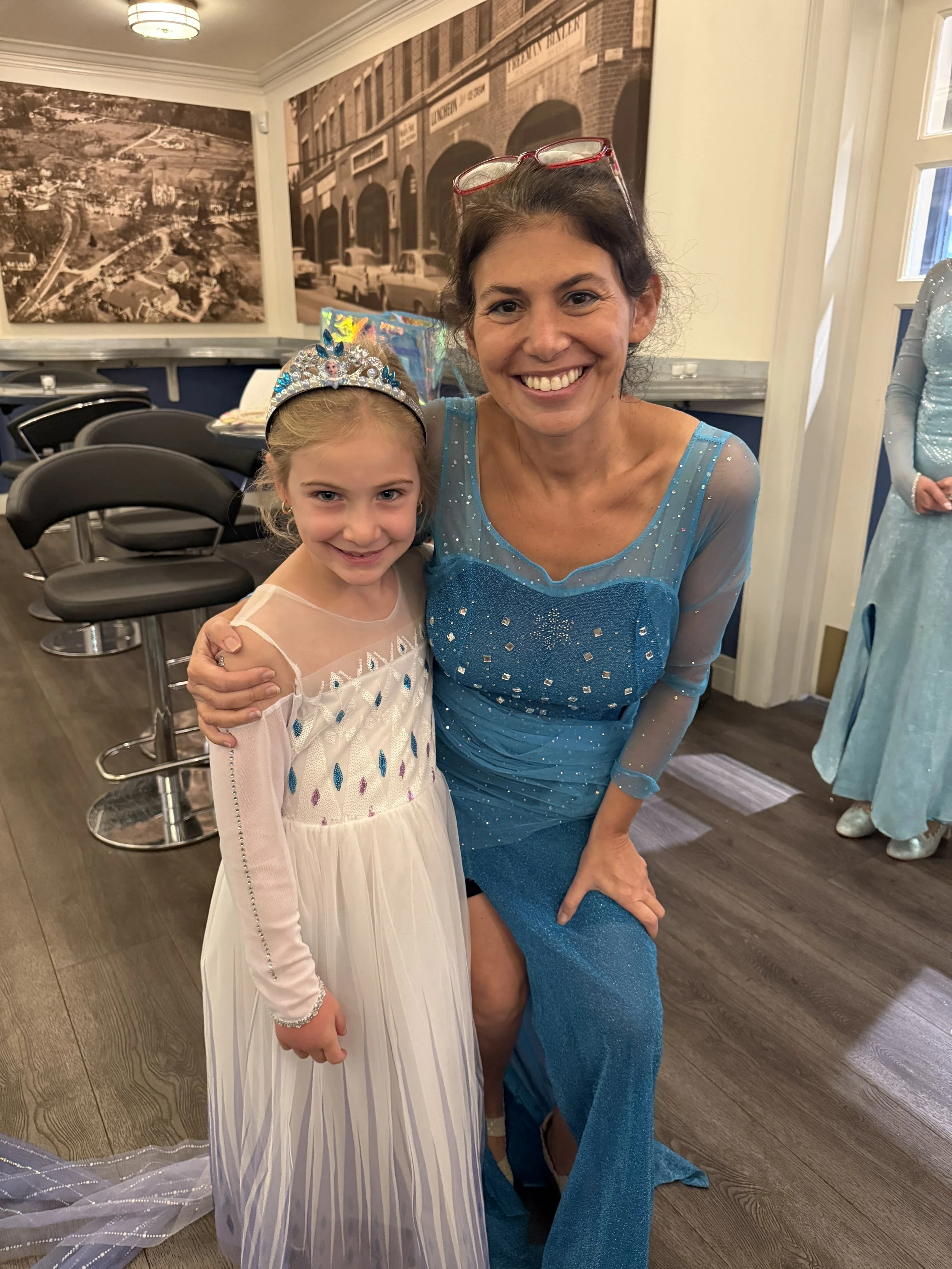 Teacher, Melissa Toole, dressed as Elsa from Frozen standing next to a young girl dressed as Elsa from Frozen, both smiling.