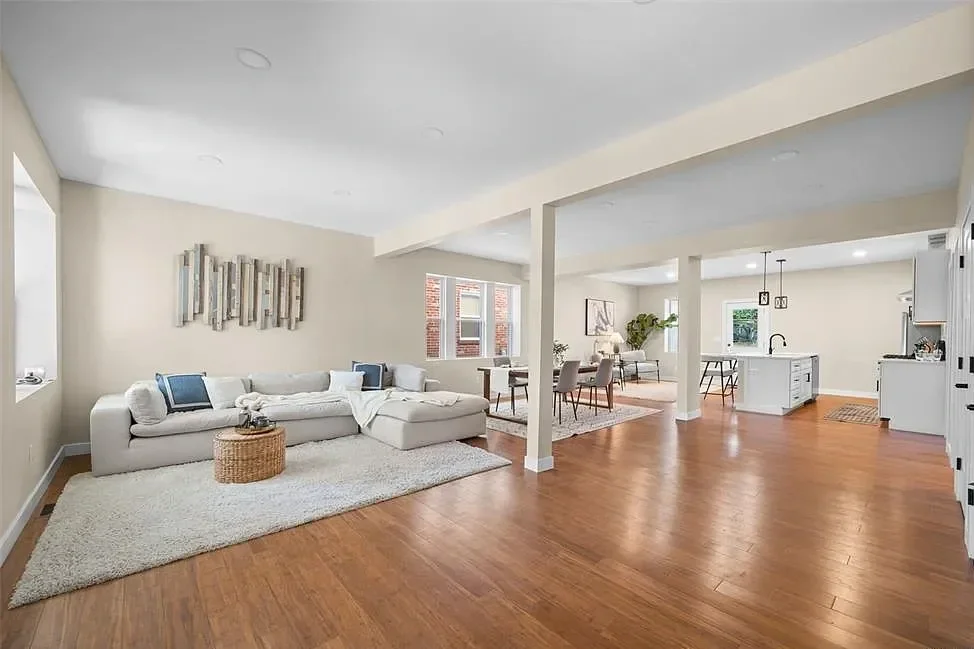 Open-concept living room, dining area, and kitchen with hardwood floors, white walls, and modern decor.