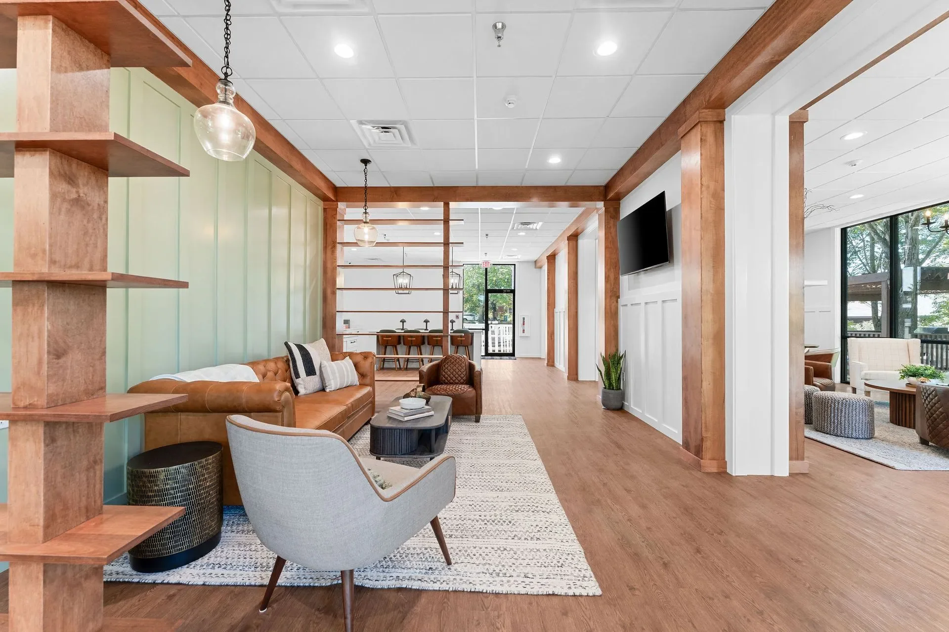 Interior of a modern lounge or waiting area with wooden accents, a leather sofa, a patterned armchair, and a flat-screen TV mounted on the wall.