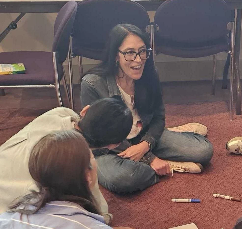 Andrea Rodgers sitting on the floor in a workshop circle, talking with participants
