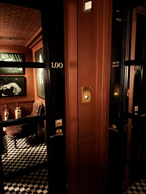 Interior of an elegantly decorated room with patterned upholstery chair, framed artwork, and checkered flooring, viewed through an open door with the room number 1004 labeled.
